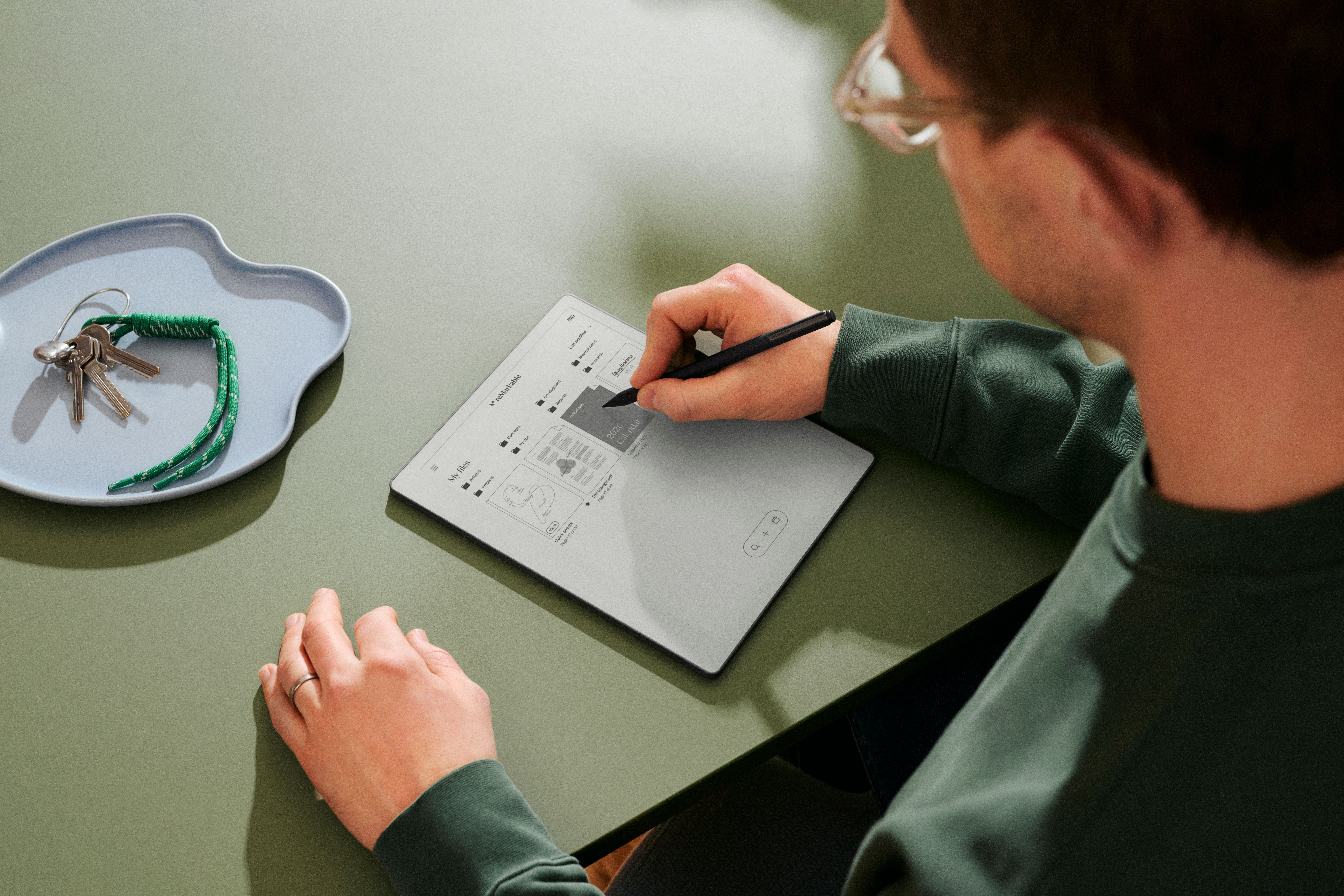 Ein reMarkable Paper Tablet, auf dem Text zu sehen ist. Daneben ein Mann, der einen Marker in der Hand hält und in der Nähe eines Fensters steht.
