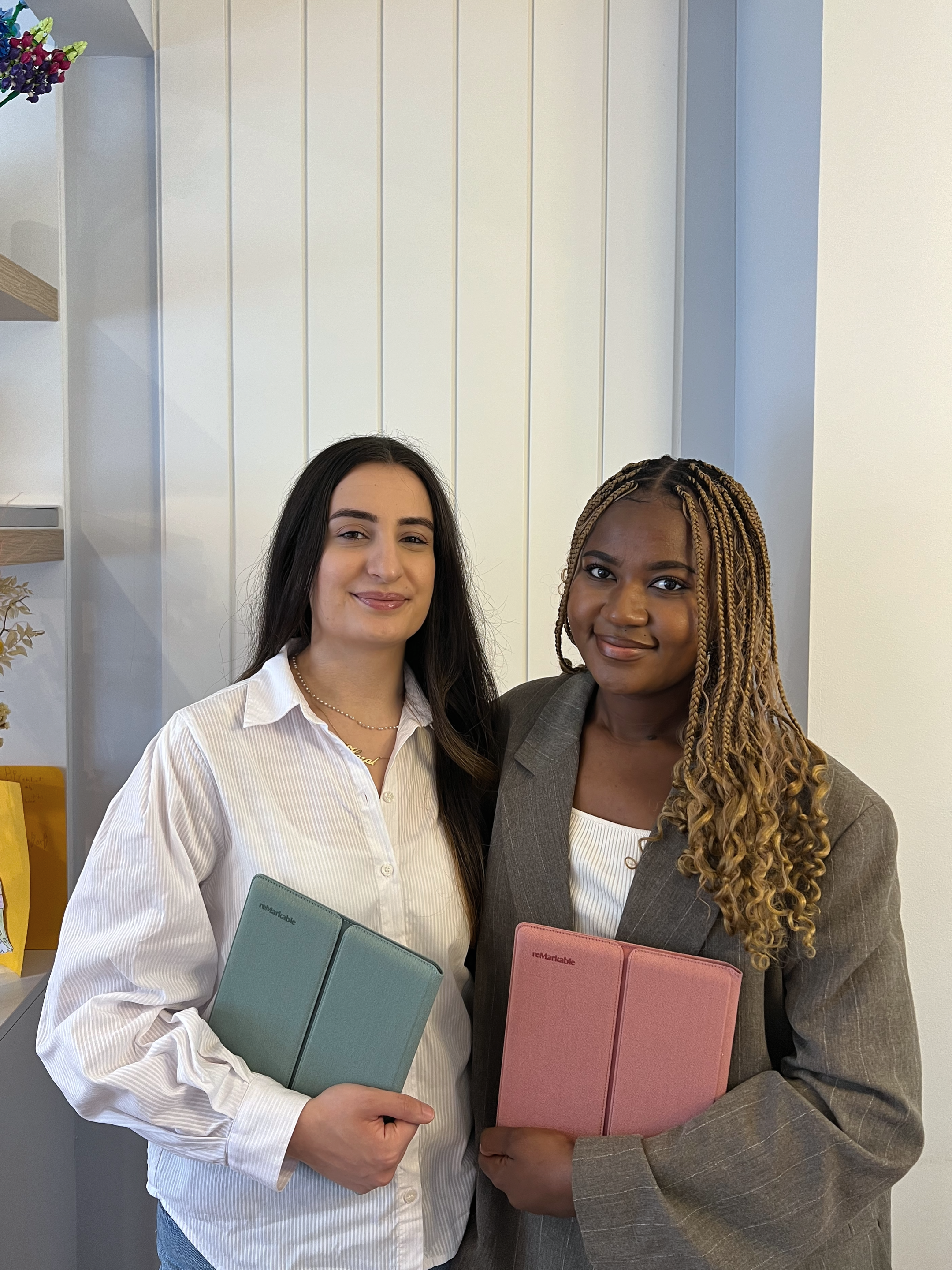 Dr. Lydie Kitenge holding a reMarkable Paper Pure tablet in a Mist Green sleeve folio, and Dr. Hazal Trench holding one in a Desert Pink sleeve folio.