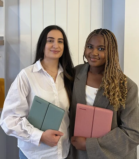 Dr. Lydie Kitenge holding a reMarkable Paper Pure tablet in a Mist Green sleeve folio, and Dr. Hazal Trench holding one in a Desert Pink sleeve folio.