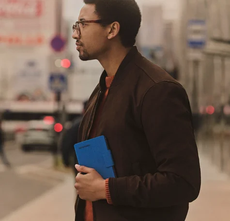 A man on the street carrying the reMarkable Paper Pro Move in a Cobalt Mosaic Weave folio
