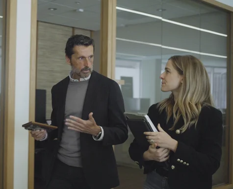 A man and woman in an office walk and talk; she holds a reMarkable paper tablet.
