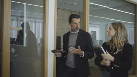 A man holding a reMarkable paper tablet while talking with a woman in an office.