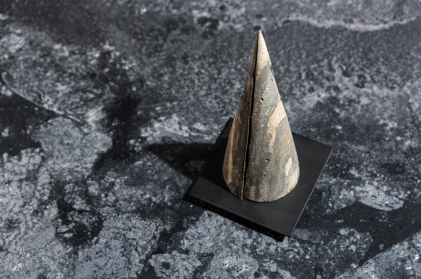 A brown and grey marbled cone sits on a floor made of stone. 