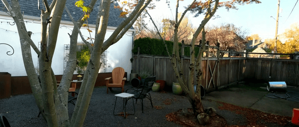 A picture of our backyard before we added anything. We have a few chairs in the middle of the yard, and we've got a fence that is old and kind of rotten. The backyard is covered in gravel and we have large cement pad as part of the patio that's next to the house.