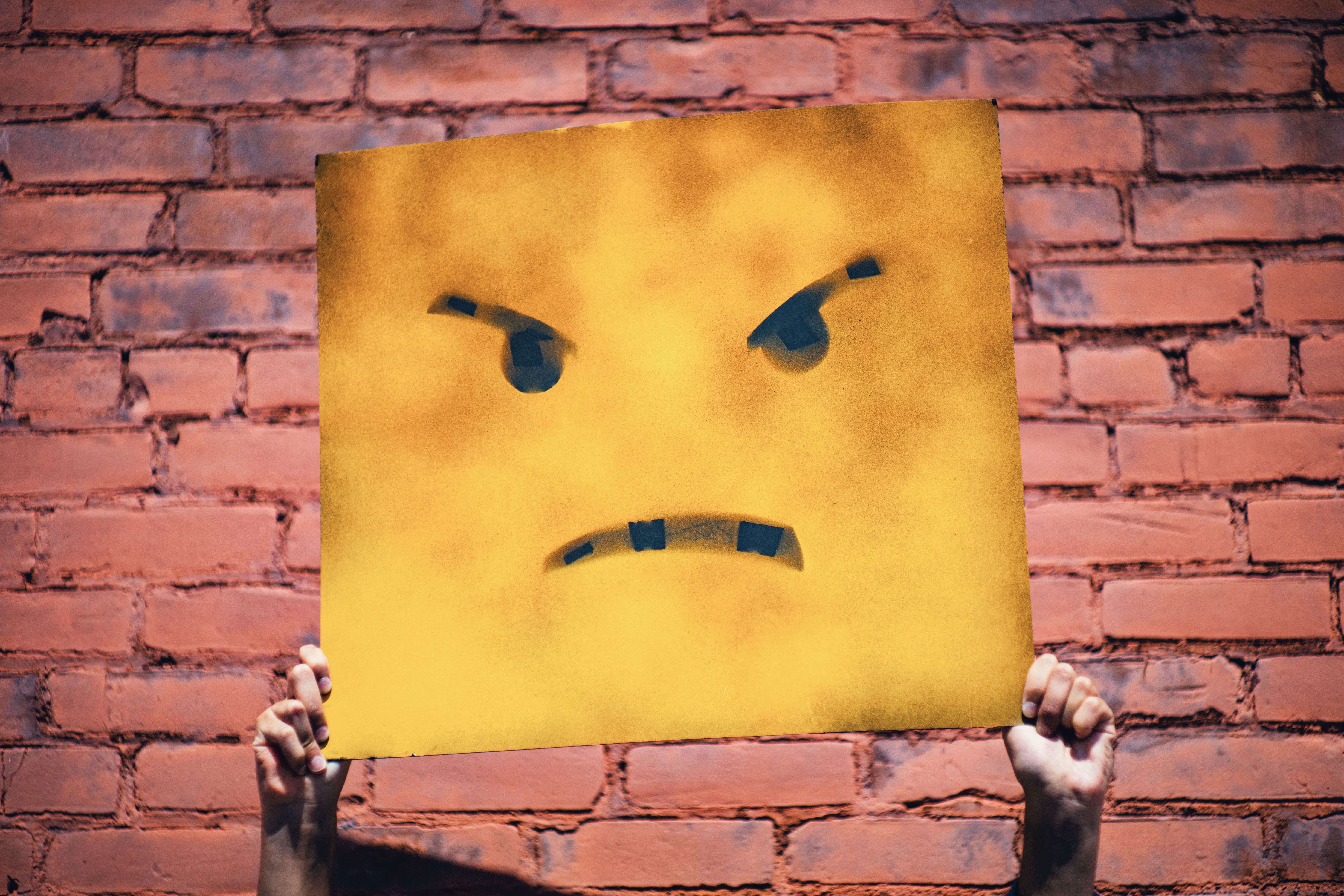 Someone holding a yellow sign that's painted with an angry face