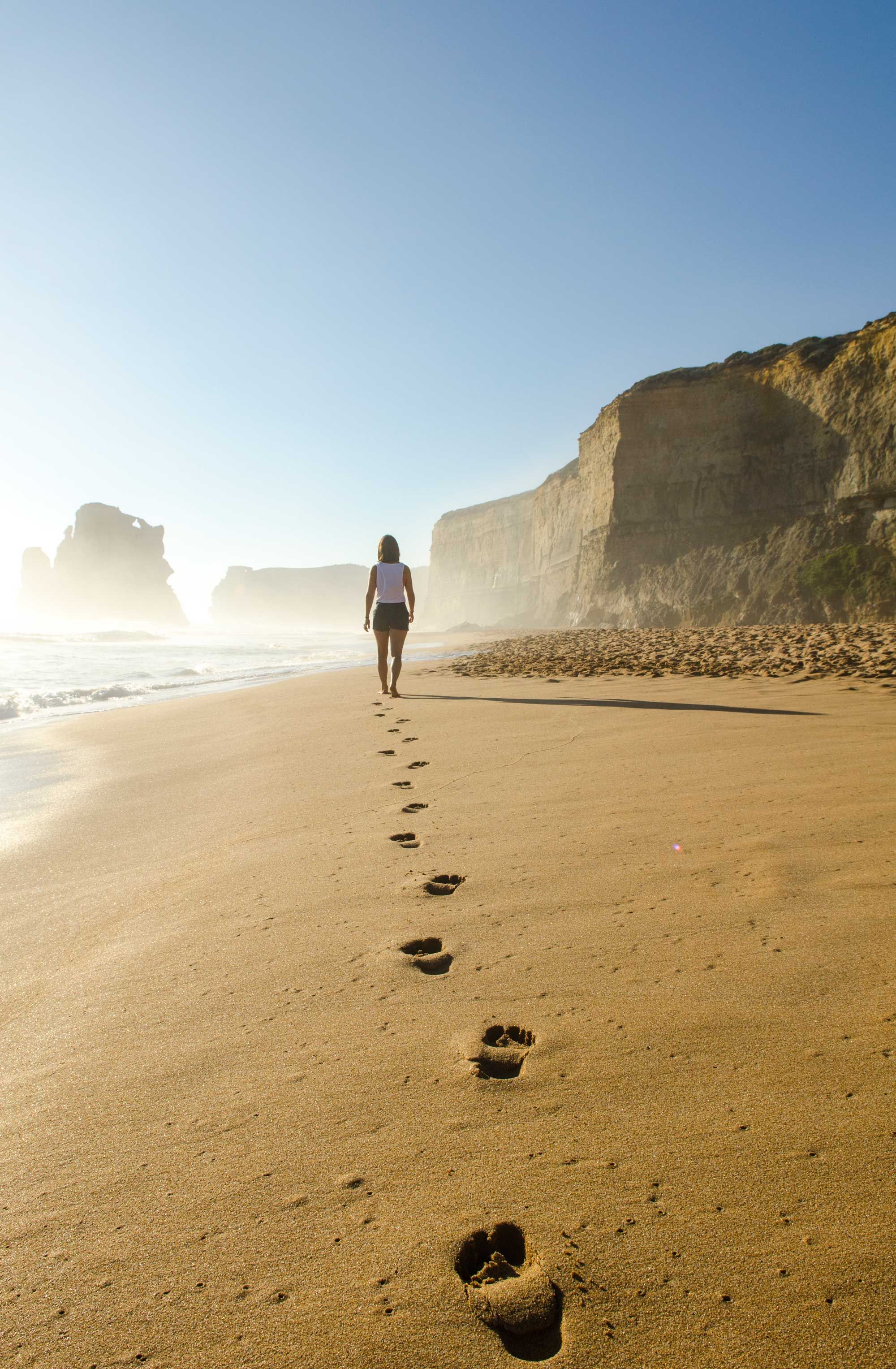 Person walking down a beach with their footprints behind them
