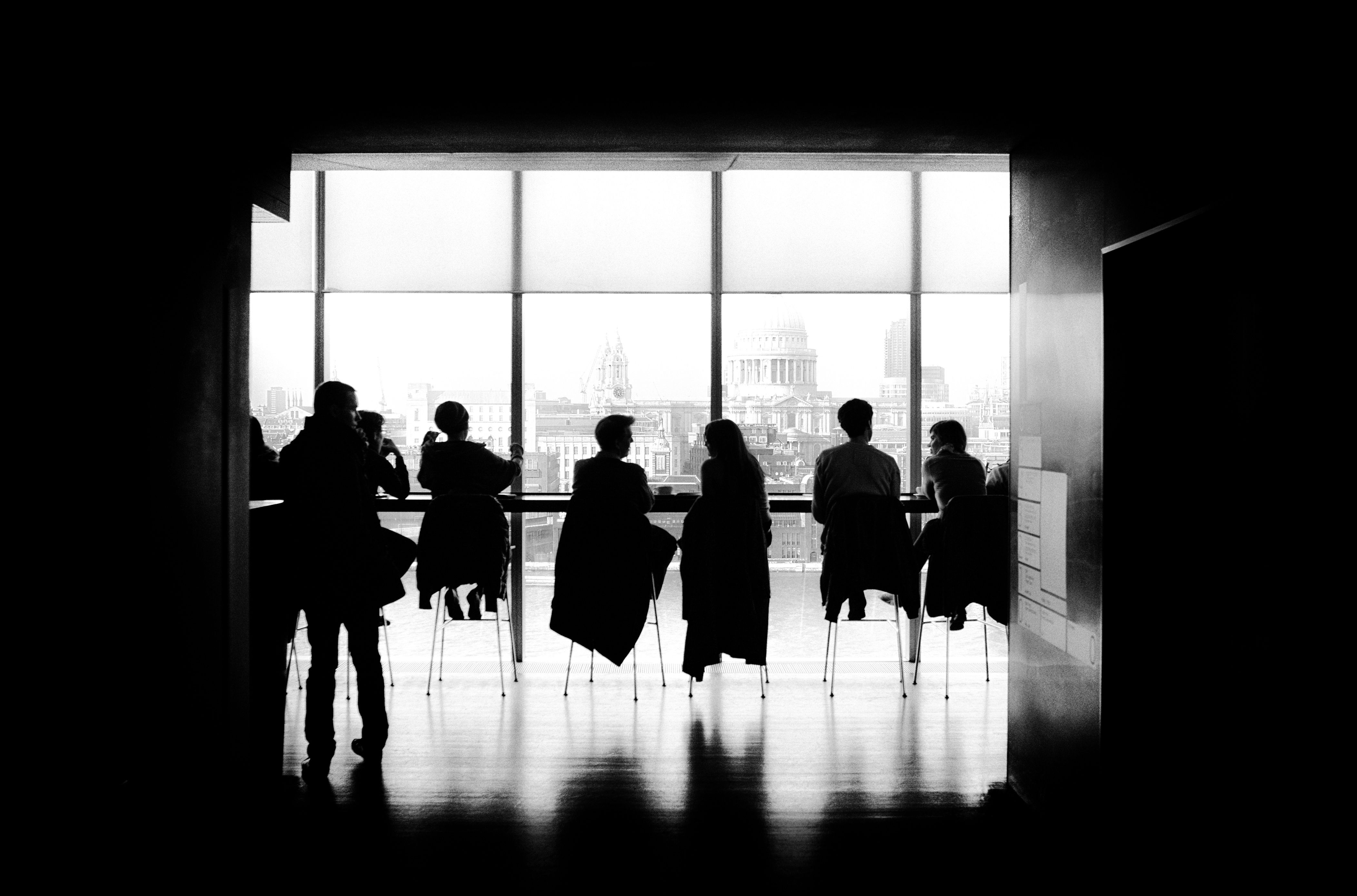 Silhouette of several people sitting in chairs at a large conference table