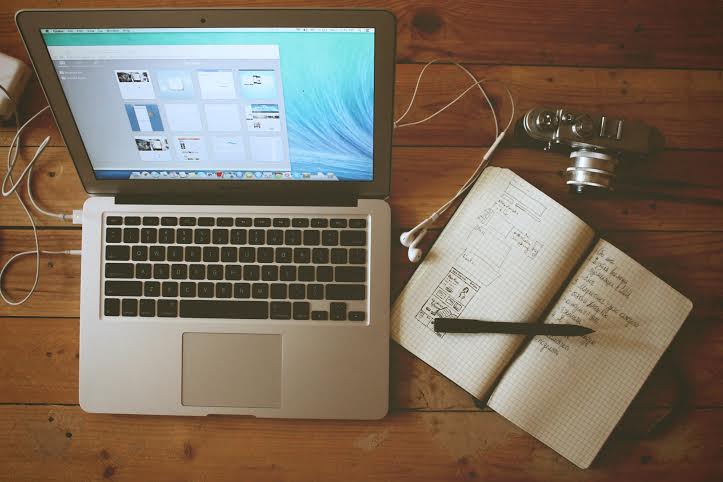 Laptop with camera, notebook with UI drawings, and a camera.