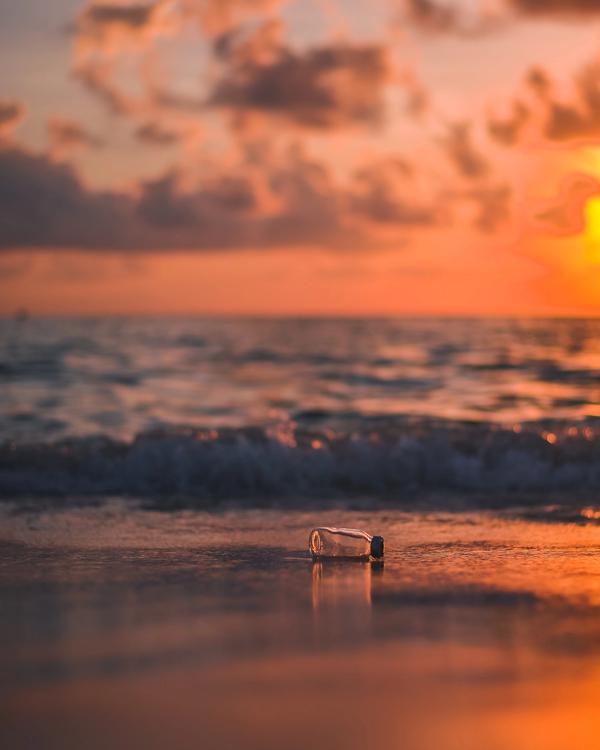 A sunset on the beach, with a plastic bottle laying on the sand.
