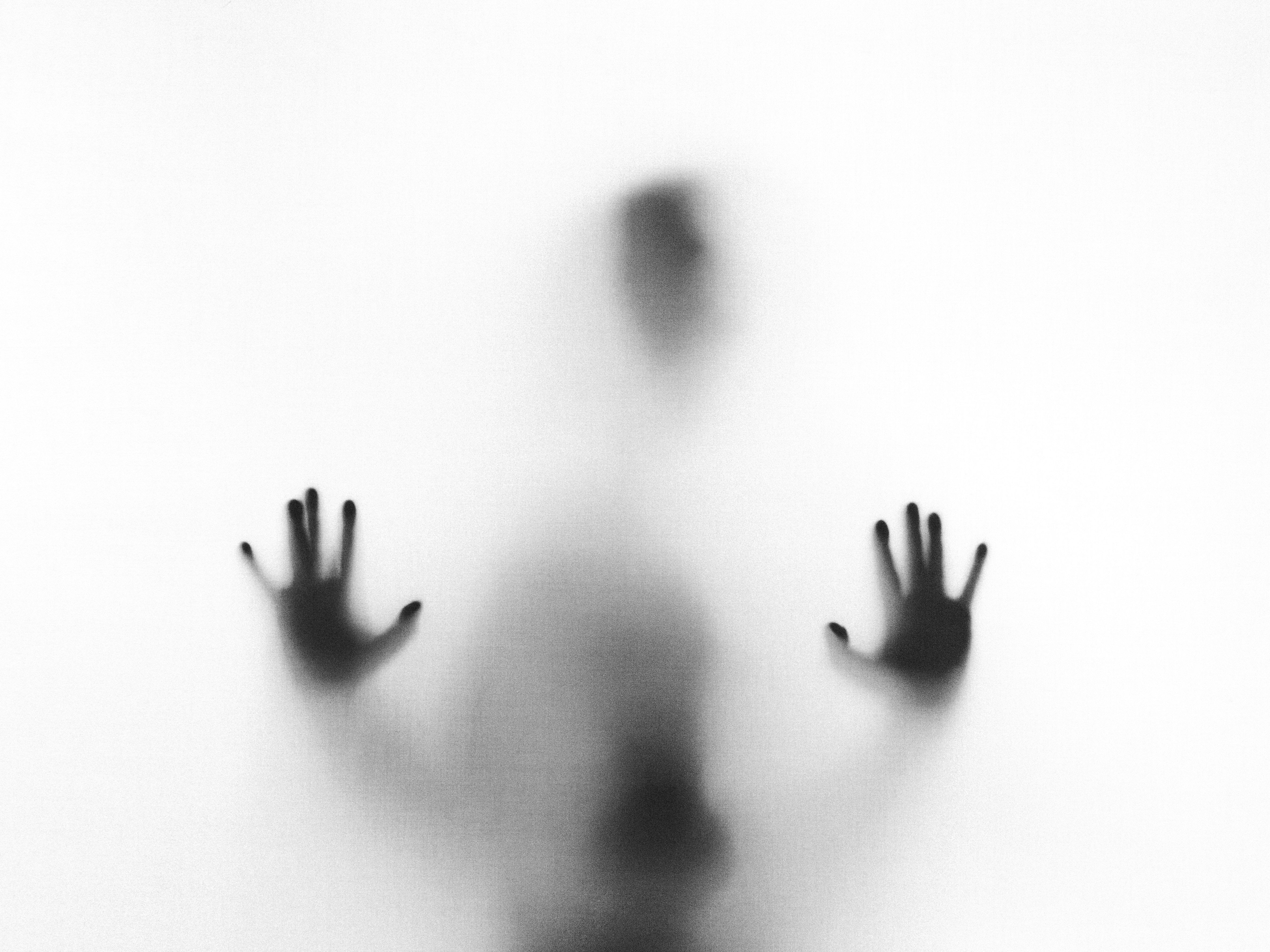 Black and white image of a silhouette standing behind fogged glass