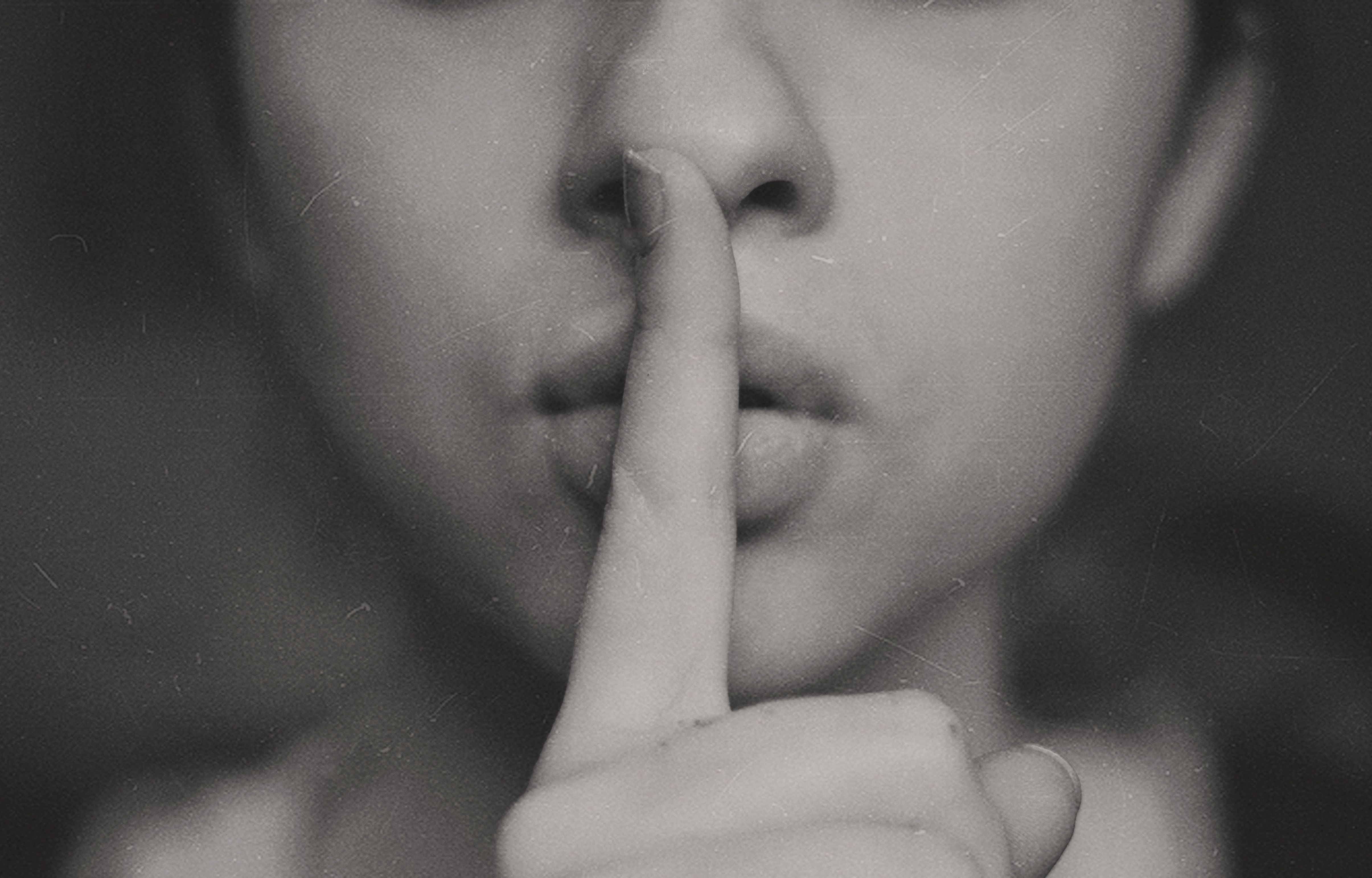 Woman making silencing motion with her finger to her lips.