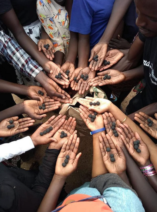 A group of people holding charcoal covered seeds from Seedballs Kenya.