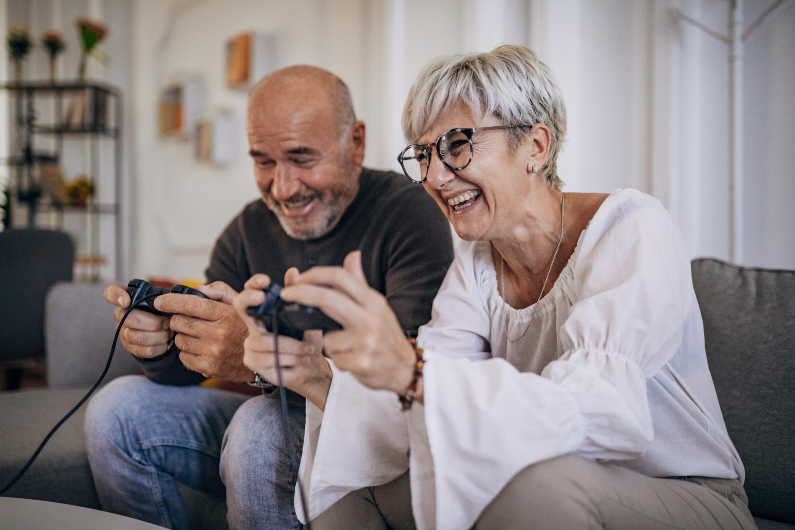 Middle-aged couple sitting on the sofa laughing and playing video games