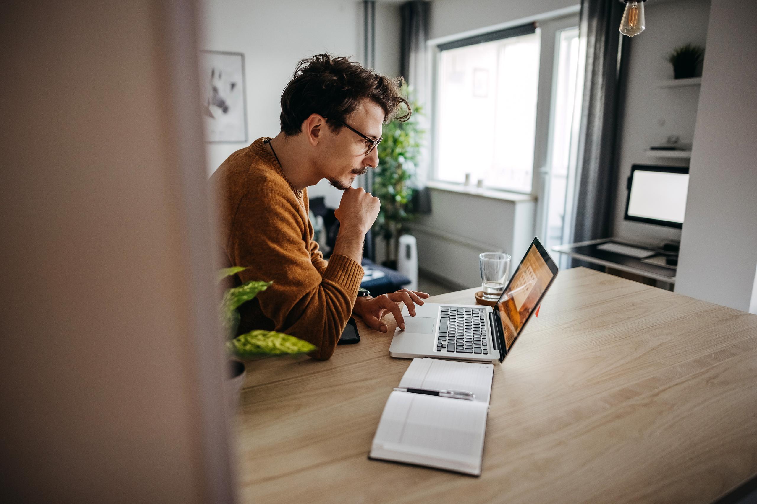a man sitting with a laptop and a notepad