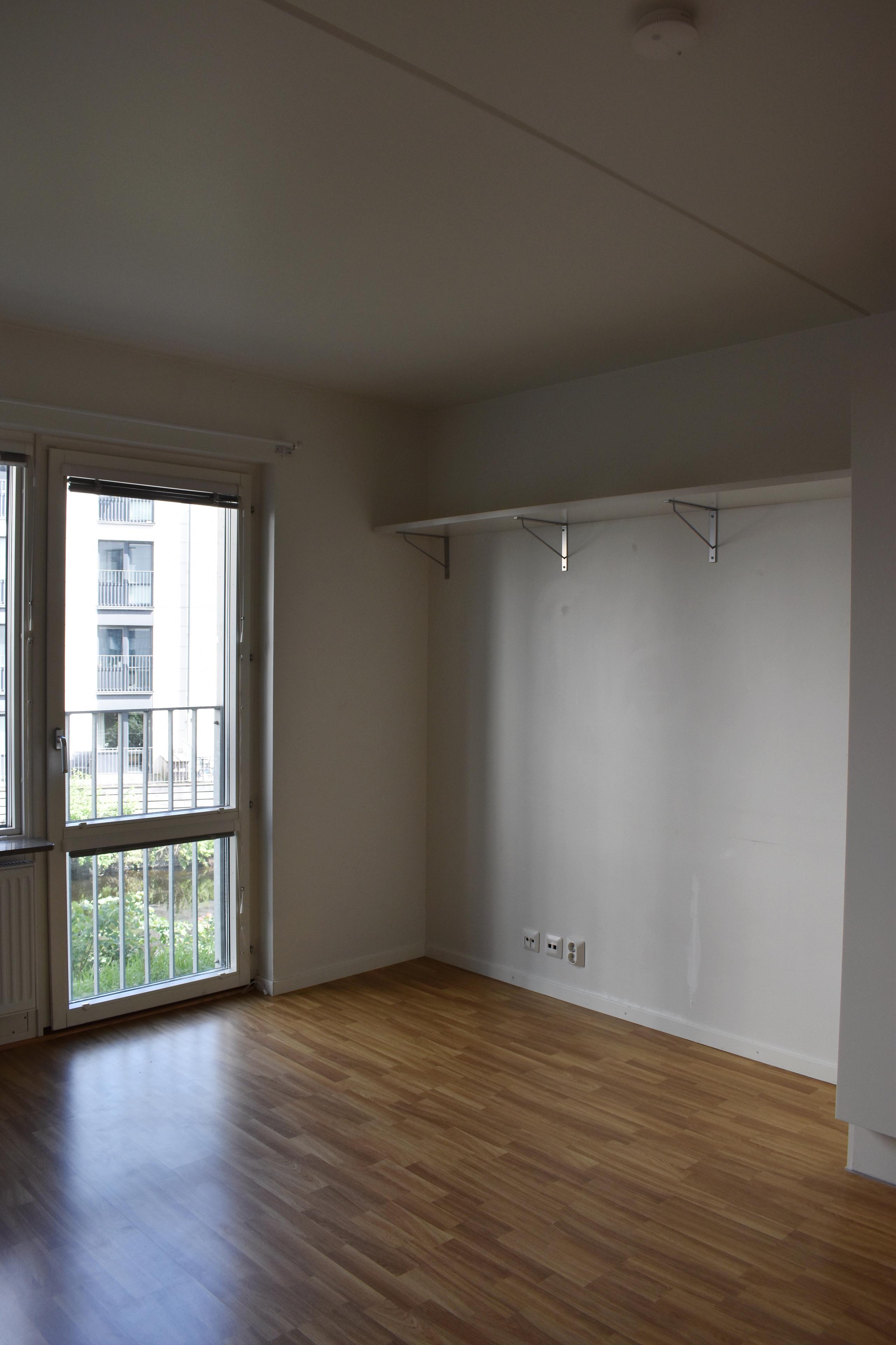Student apartment. White walls and oak parquet. Balcony door with a window. A white shelf on the wall.