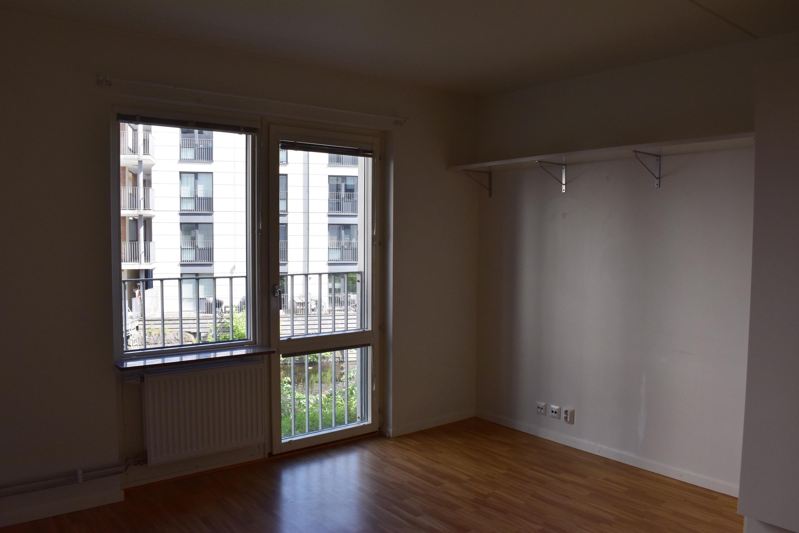 Student apartment. White walls and oak parquet. Balcony door with a window and another window beside it. A white shelf on the wall.
