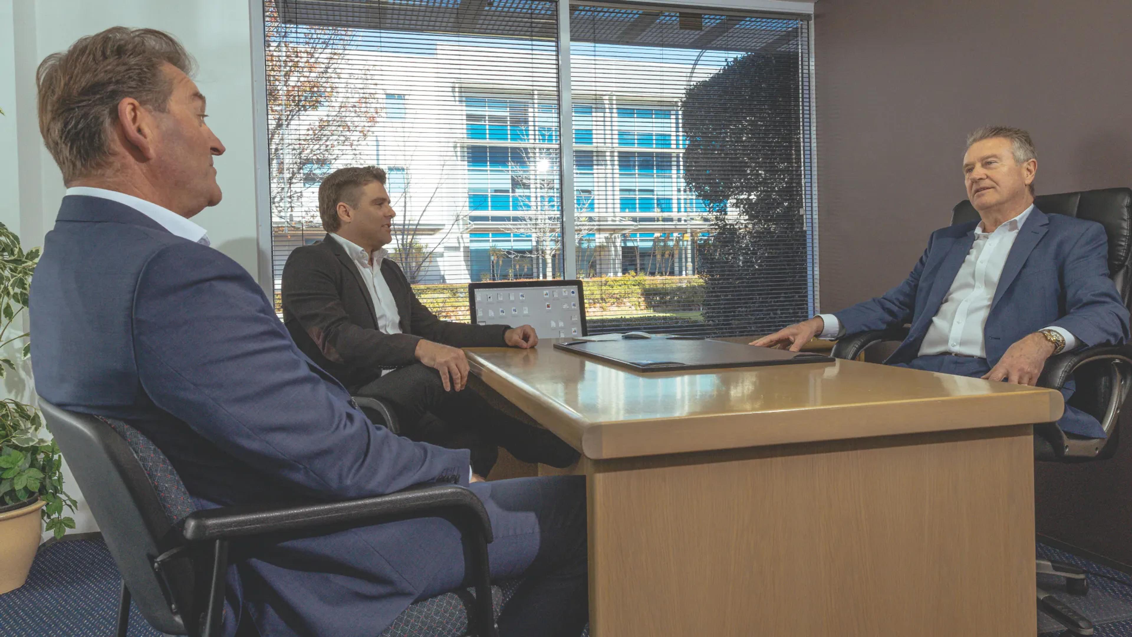 A photo of 3 men sitting at an office table taling.