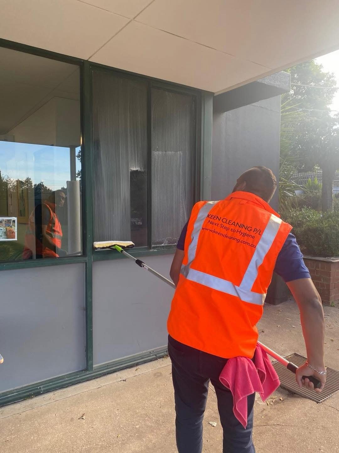 Keen Cleaning technician washing exterior windows in a branded high-visibility vest