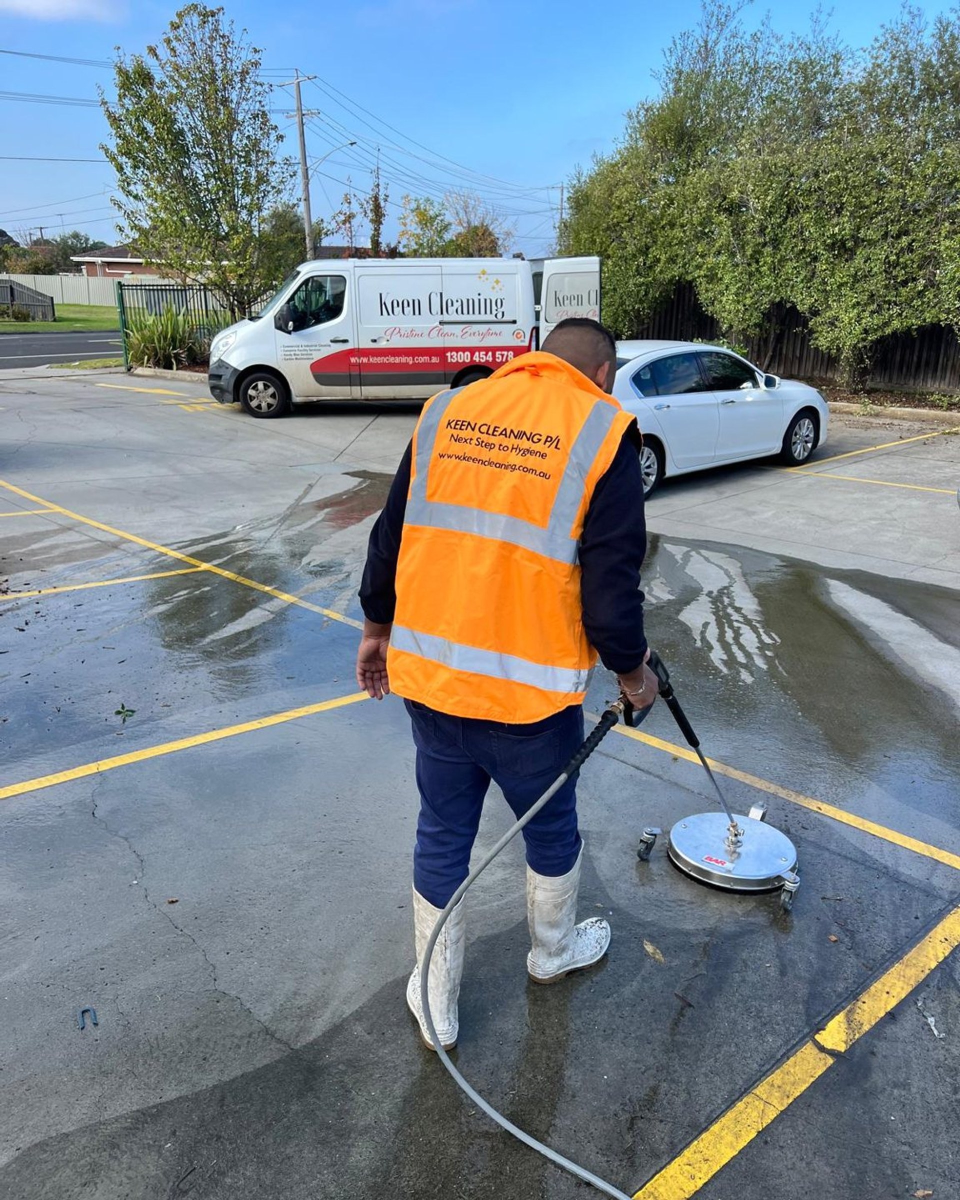 Keen Cleaning technician pressure-washing a car park with the branded van behind