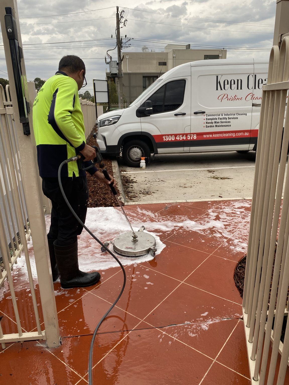 Surface cleaner foam-washing red outdoor tiles beside a Keen Cleaning van