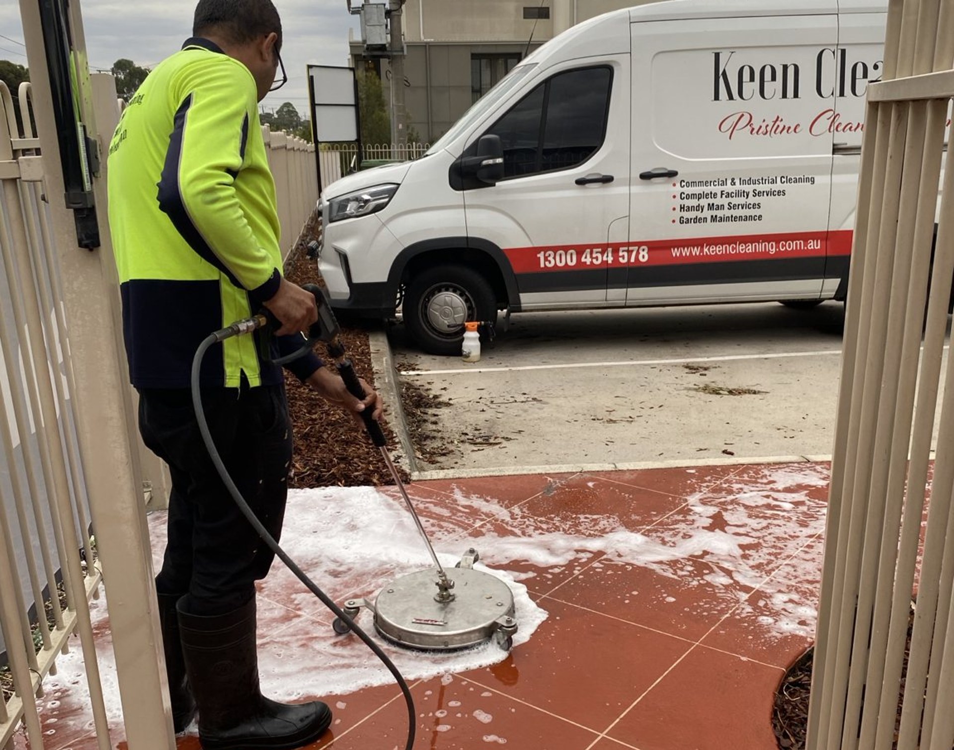 Surface cleaner foam-washing red outdoor tiles beside a Keen Cleaning van