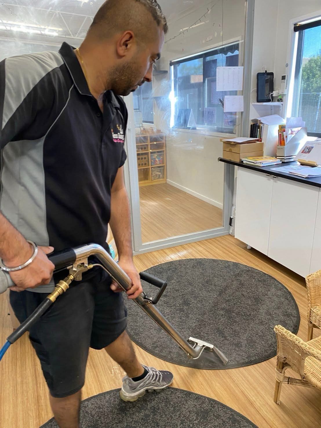 Technician steam-cleaning a rug with a professional carpet wand