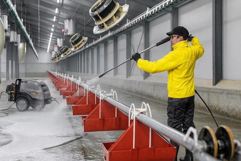 Sanitation worker in PPE deep cleaning stainless steel meat processing equipment