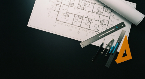 Overhead photograph of an architect's drafting table with a phased engineering blueprint, drafting tools, and a single cyan marker line