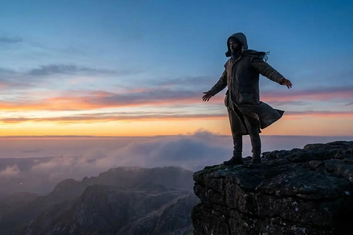 Figure facing open horizon on a cliff at sunrise, steady and resolute.
