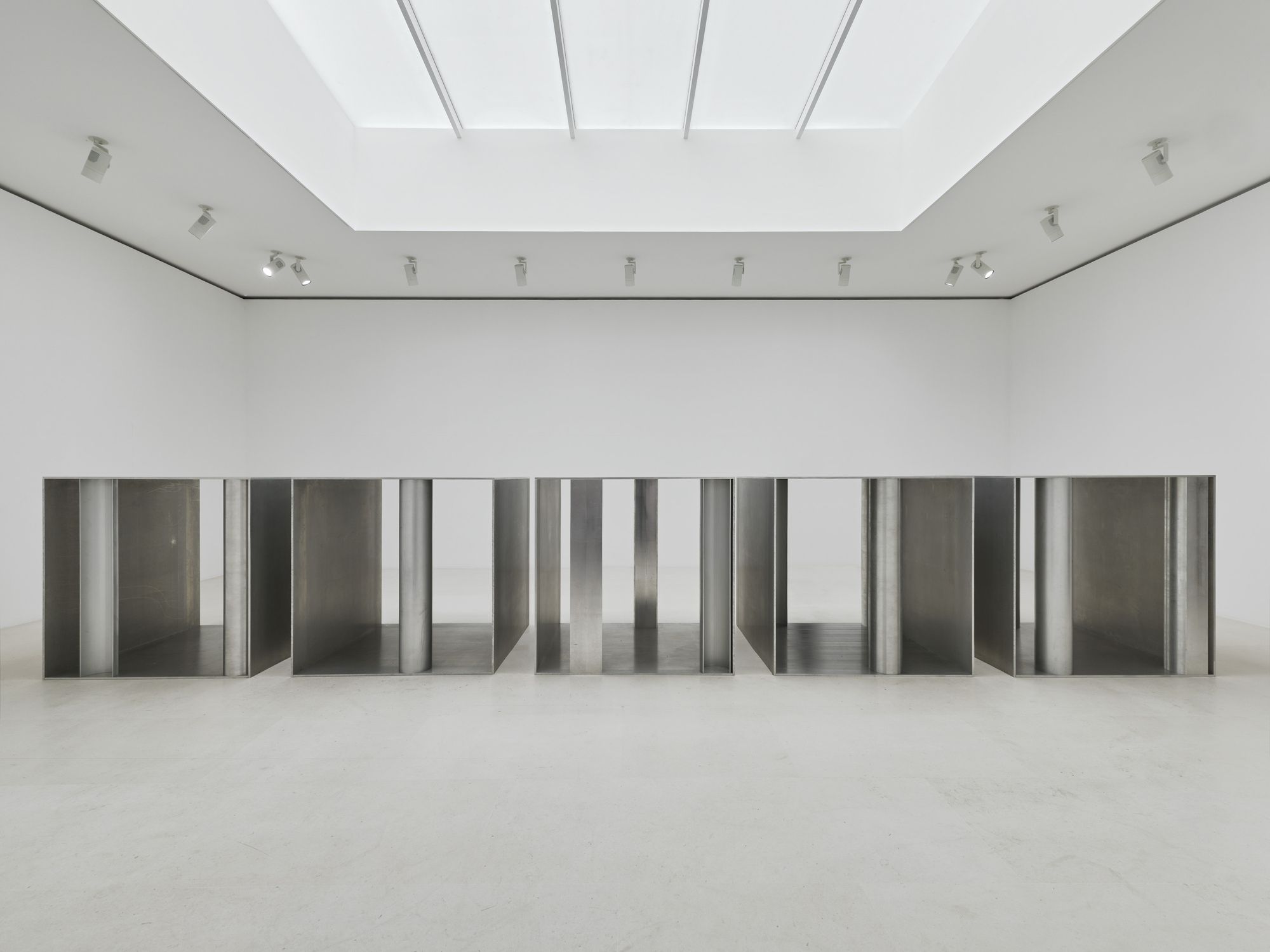 Sala blanca iluminada desde el techo, con una instalación de paneles metálicos.