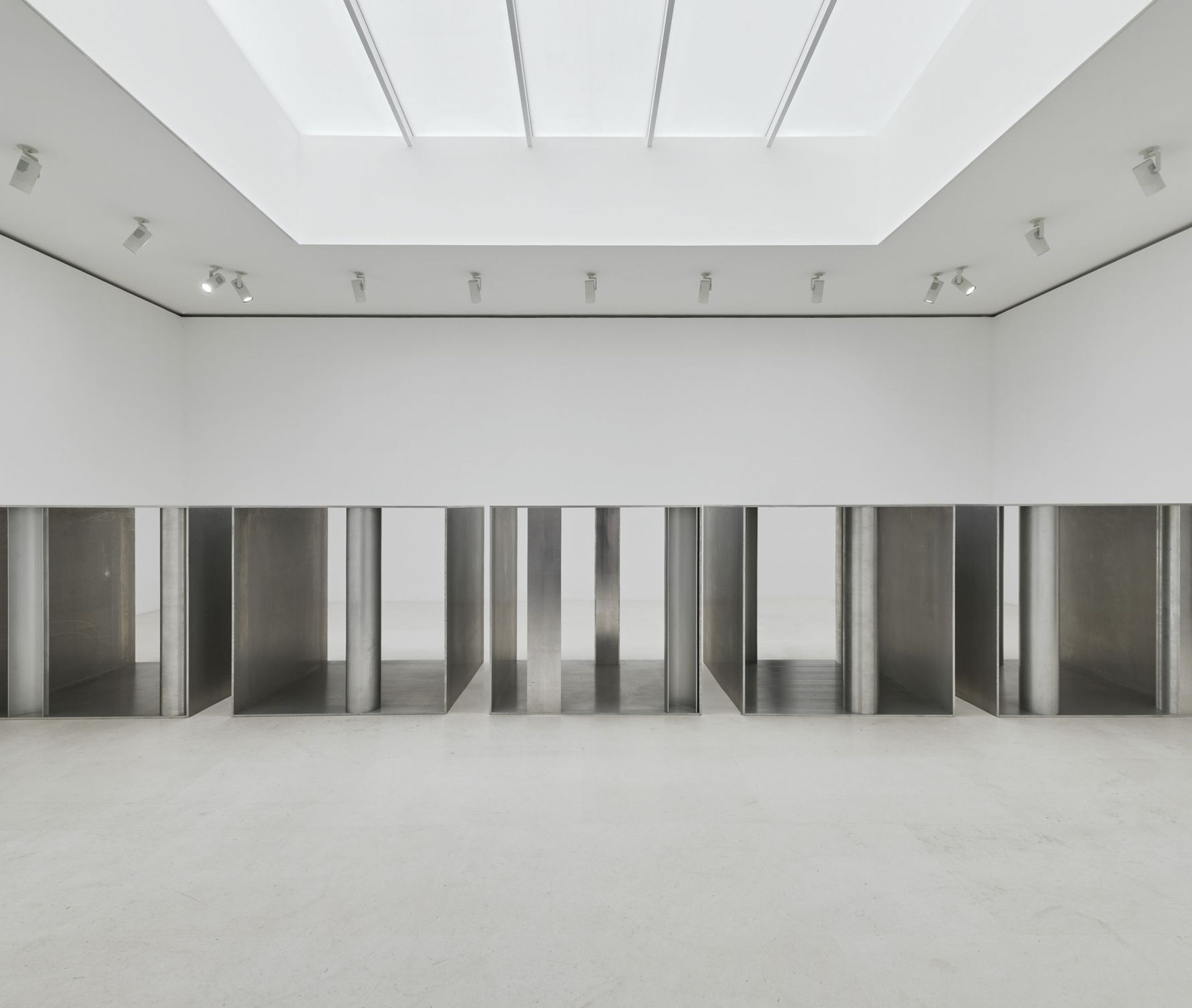 Sala blanca iluminada desde el techo, con una instalación de paneles metálicos.