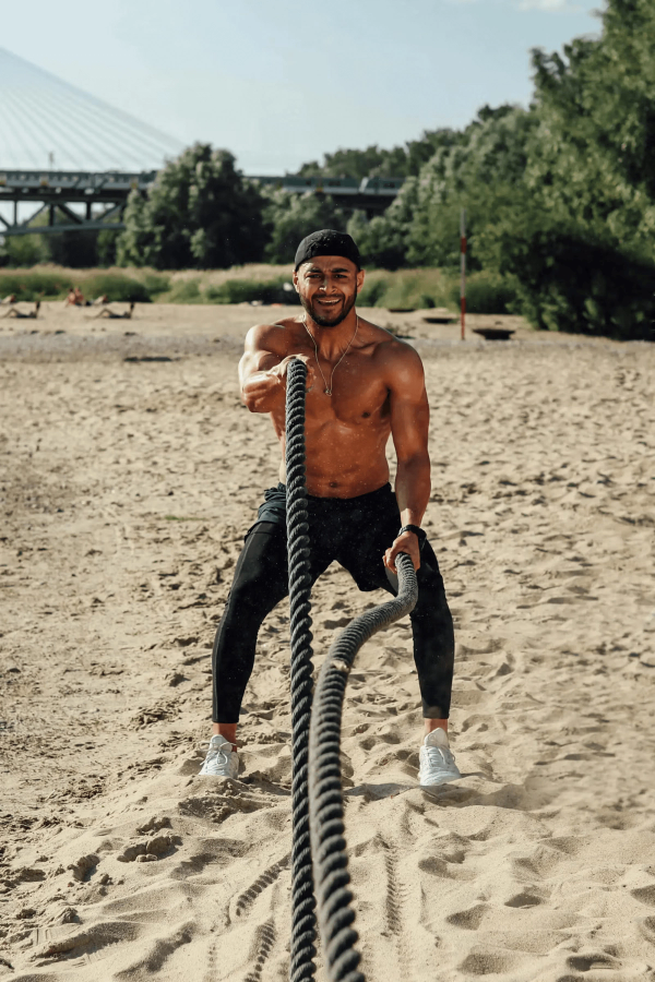 Man performing battle rope exercises on a beach