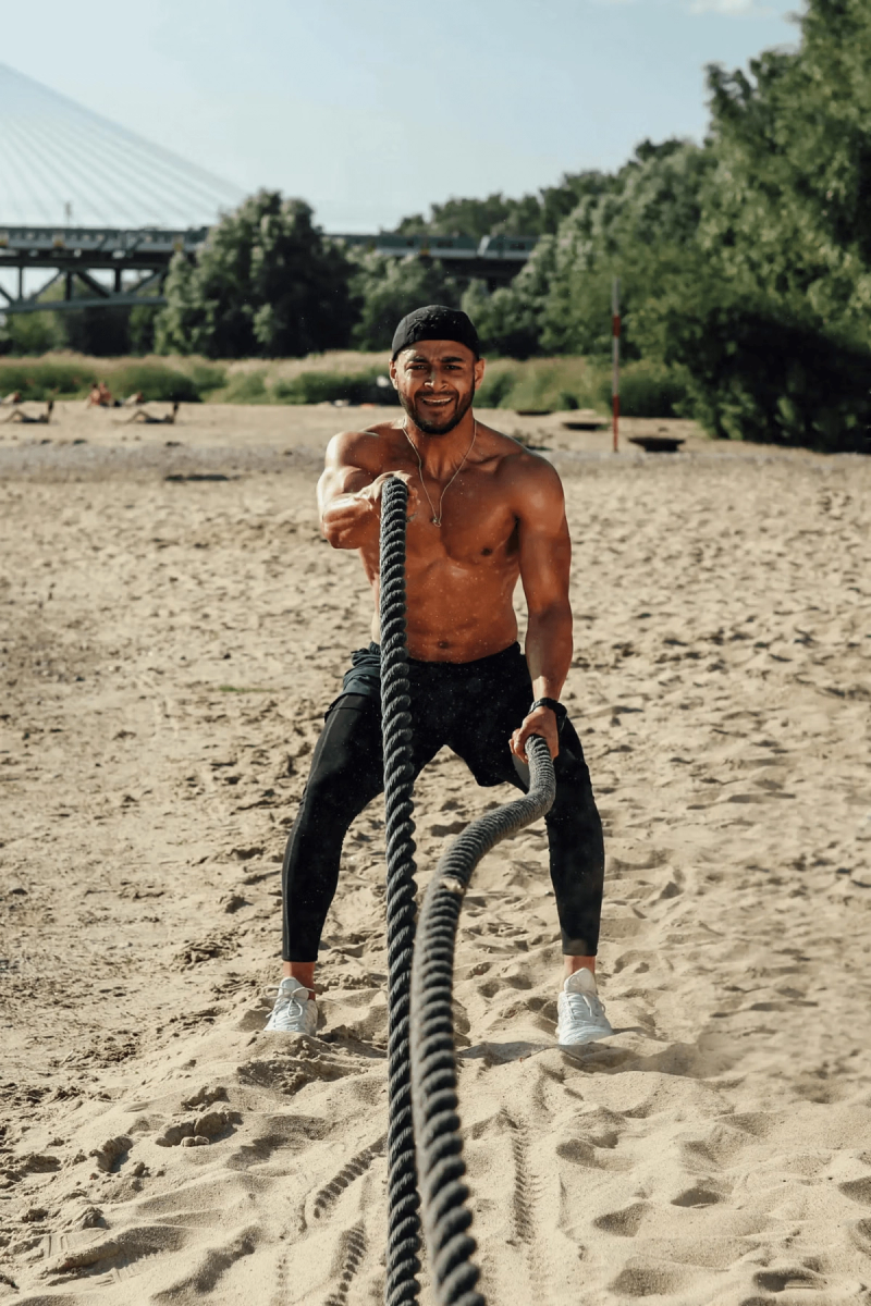 Man performing battle rope exercises on a beach