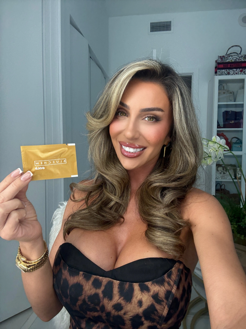 brunette lauren blake in a leopard top holding bluechew gold packet smiling