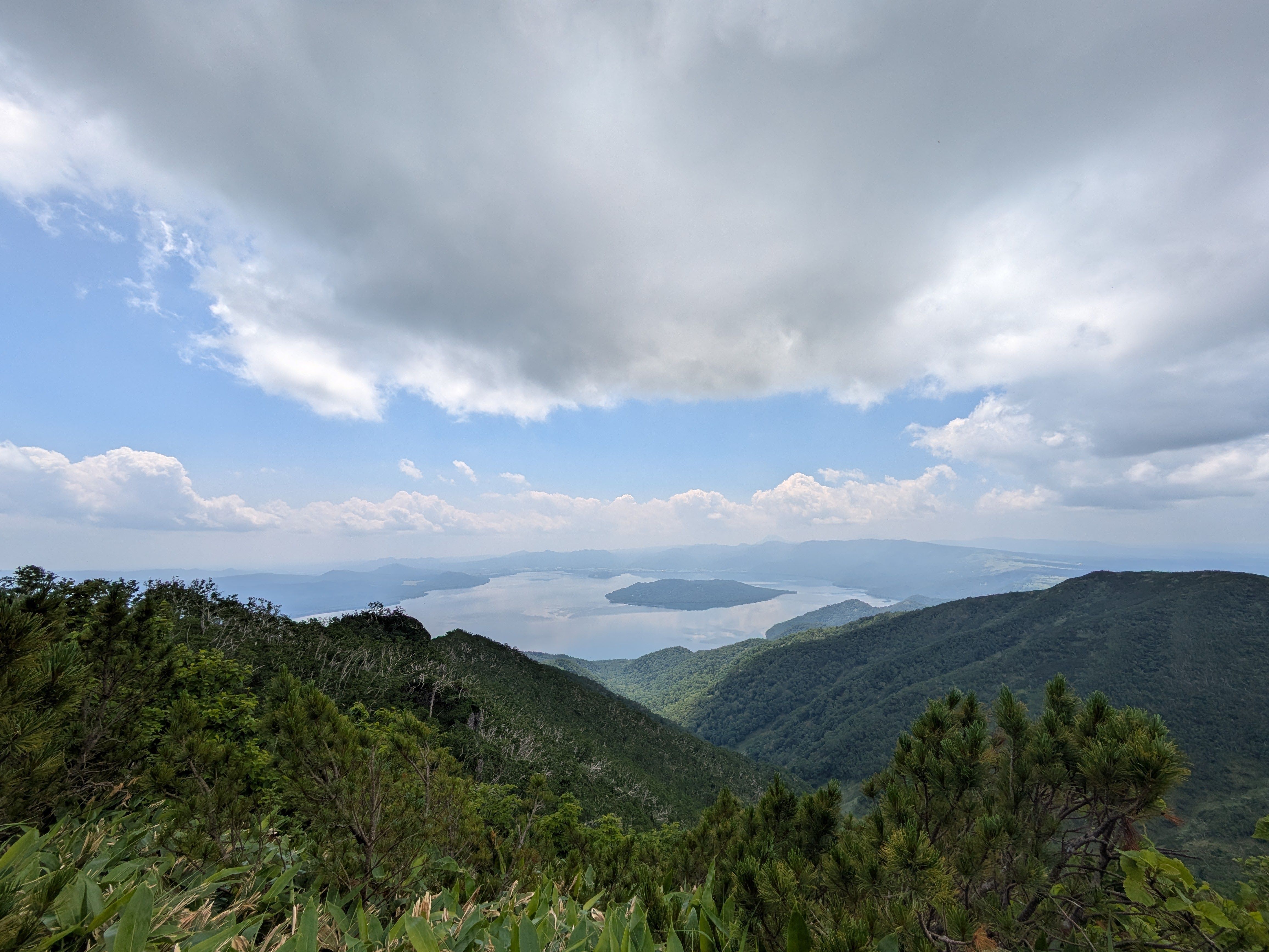 A view of Lake Kussharo in Hokkaido, Japan. It is a partially cloudy day but still, so the clouds are reflected perfectly on the lake surface.