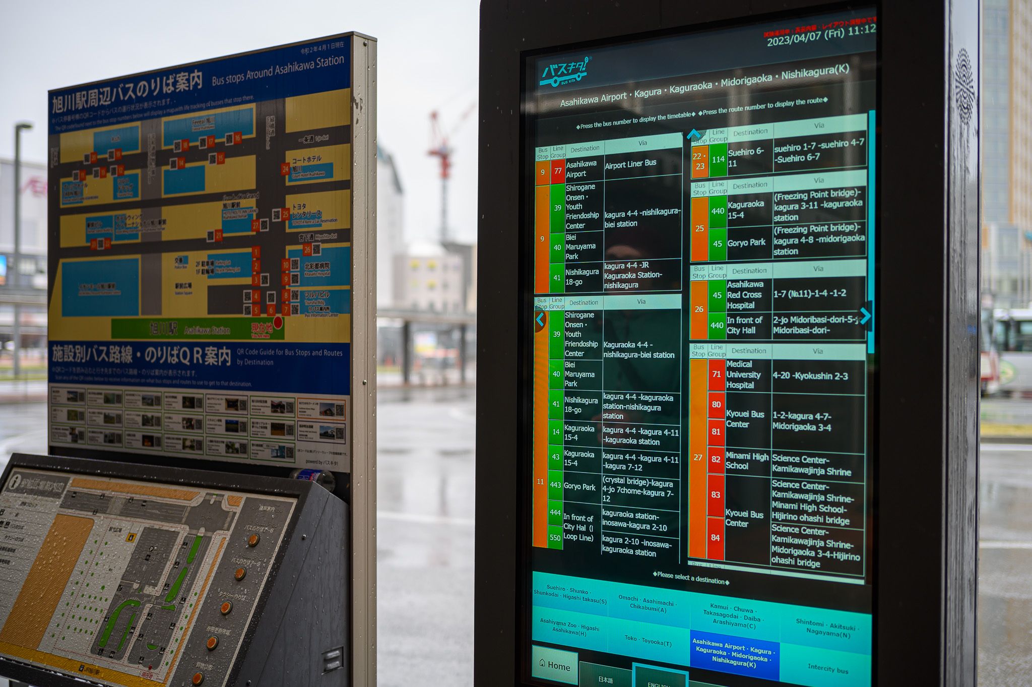 A bus timetable on an electric billboard at Asahikawa Station, next to a map showing where bus stops are relative to the reader.