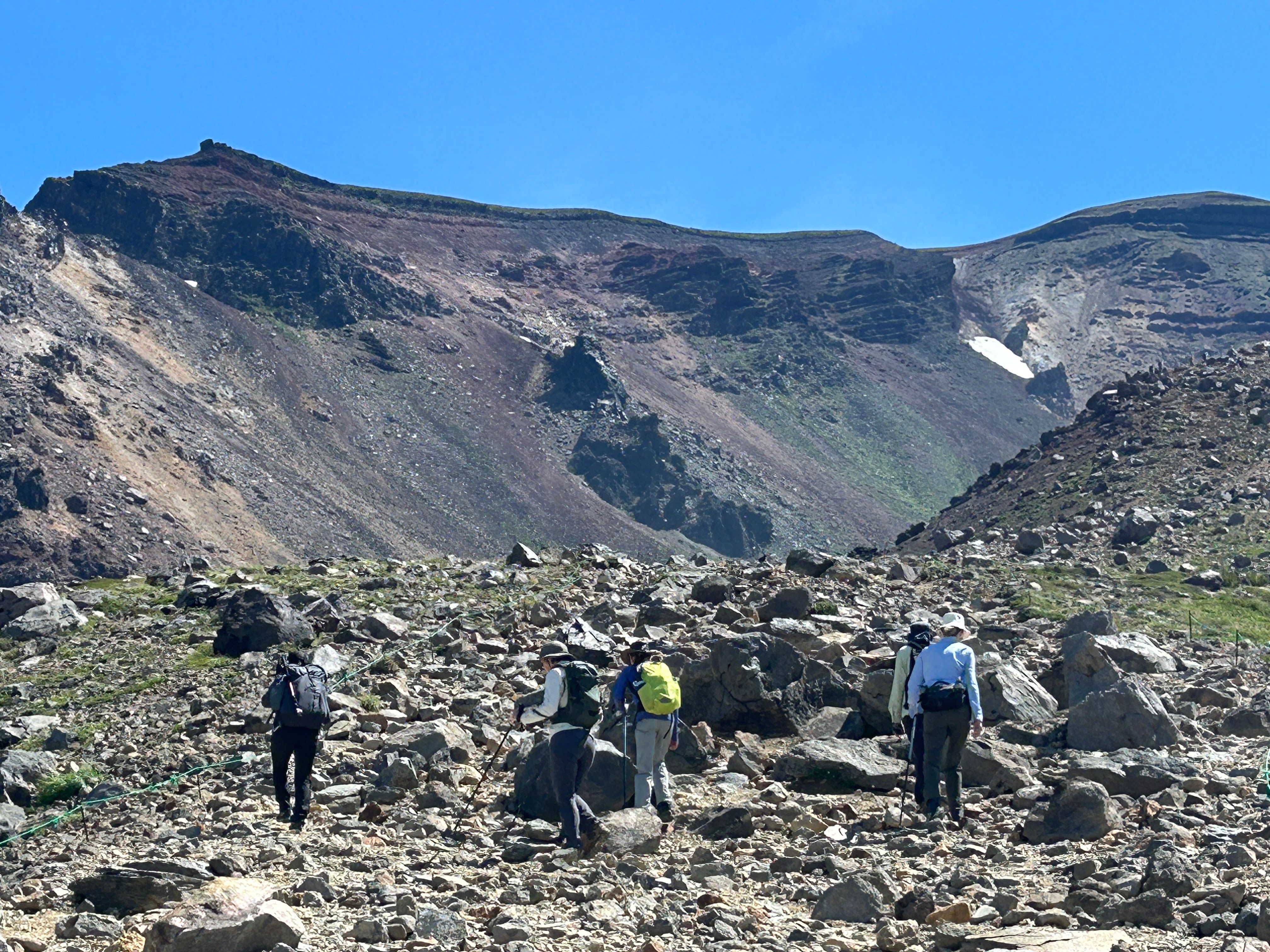 A group of hikers climb up the rocky ascent on Mt. Asahidake, Hokkaido. The trail is very rocky. It is a very sunny day.