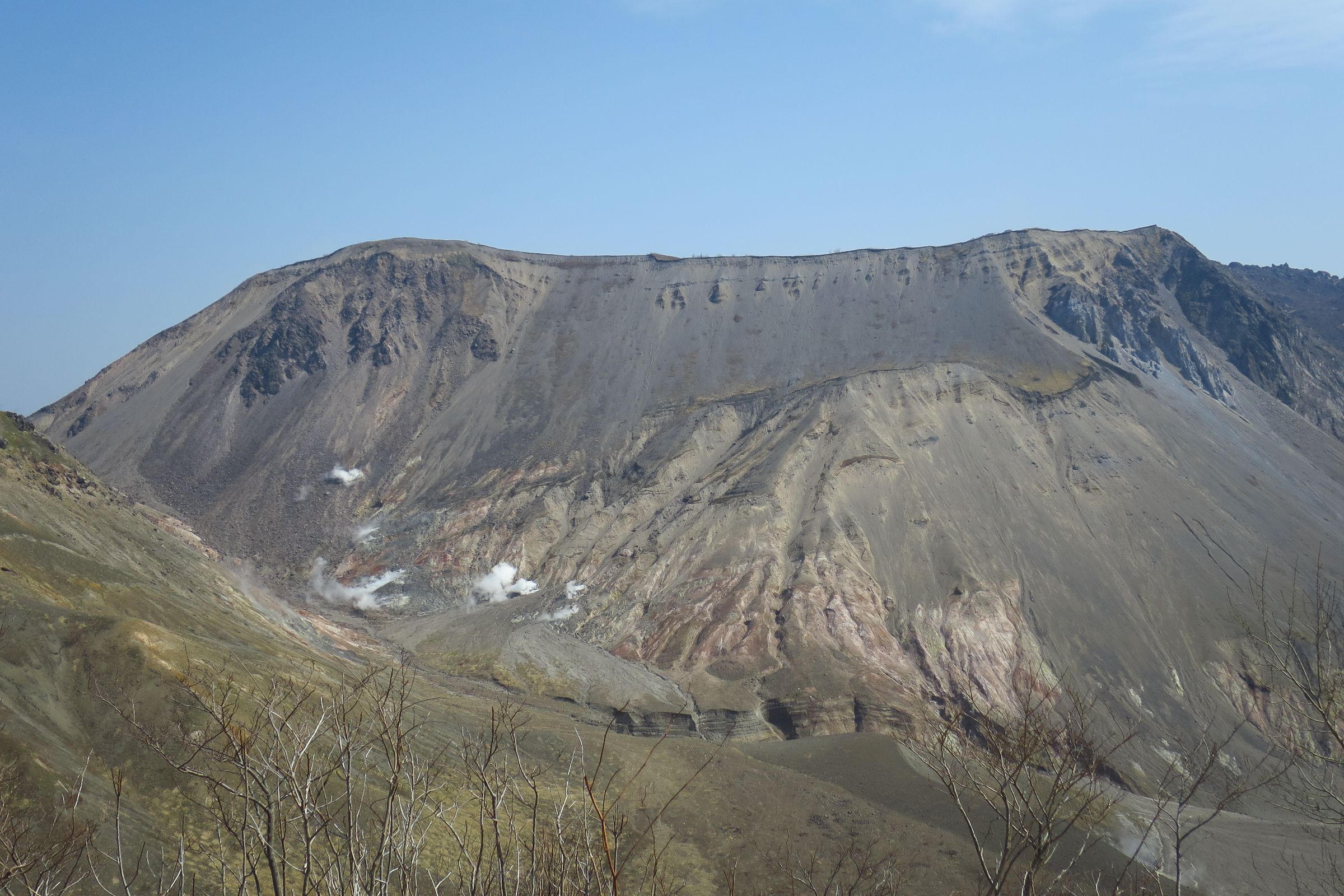 View from a crater rim overlooking the massive, steaming slopes of Mount Usu volcano in Hokkaido, featuring grey rock walls and mineral deposits.