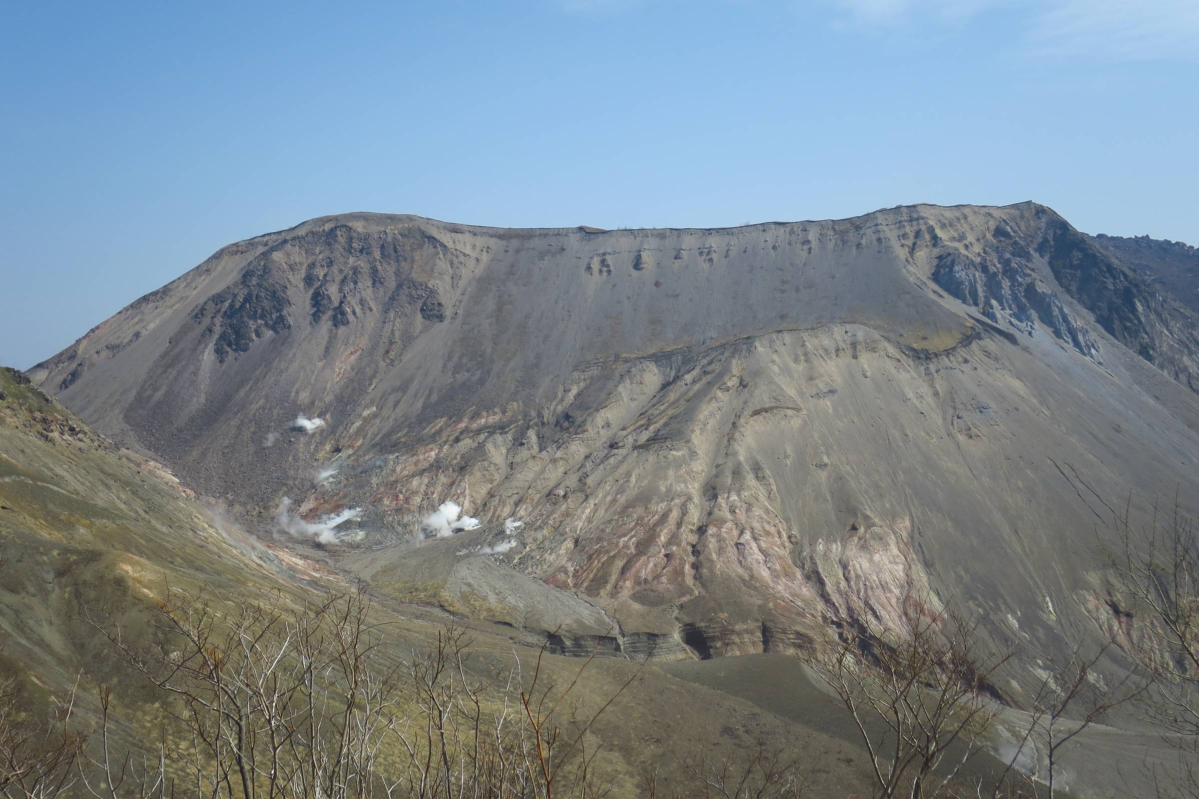View from a crater rim overlooking the massive, steaming slopes of Mount Usu volcano in Hokkaido, featuring grey rock walls and mineral deposits.