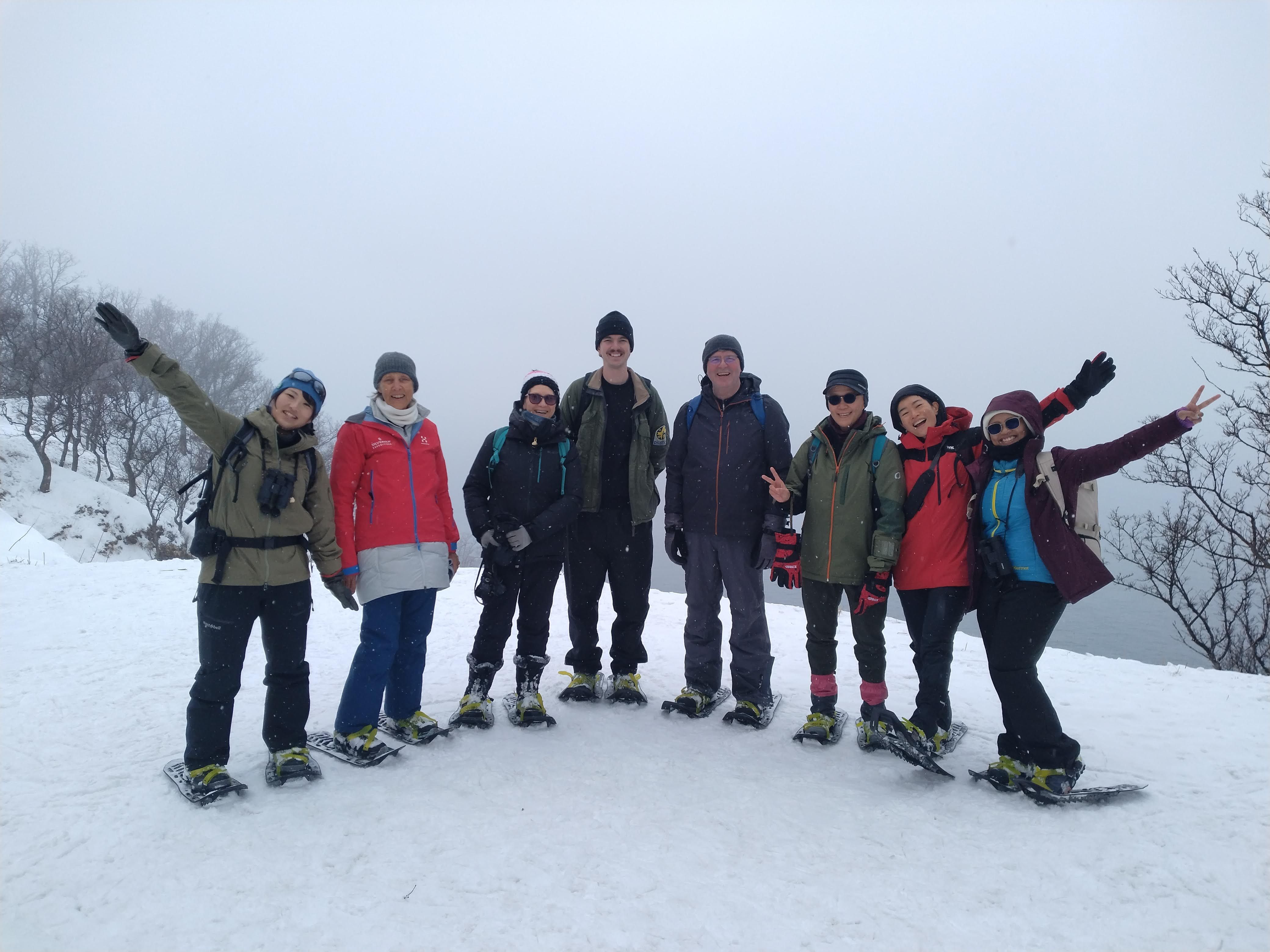 A group of people wearing snowshoes on an overcast winter day pose and smile for the camera.