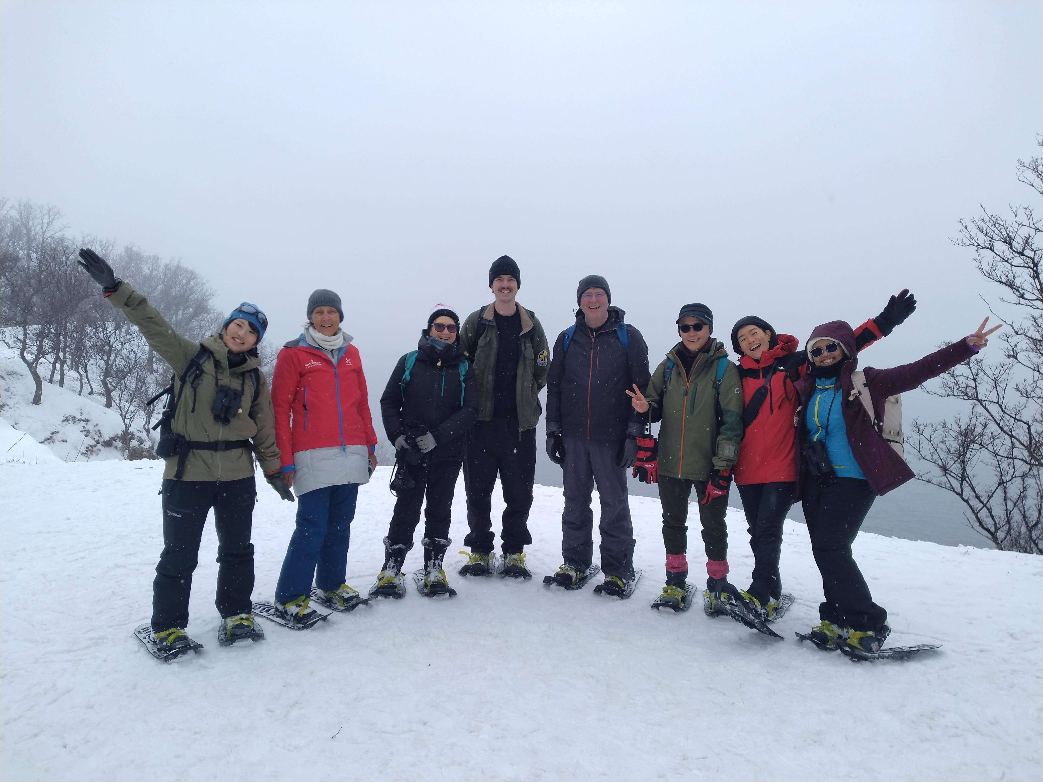 A group of people wearing snowshoes on an overcast winter day pose and smile for the camera.