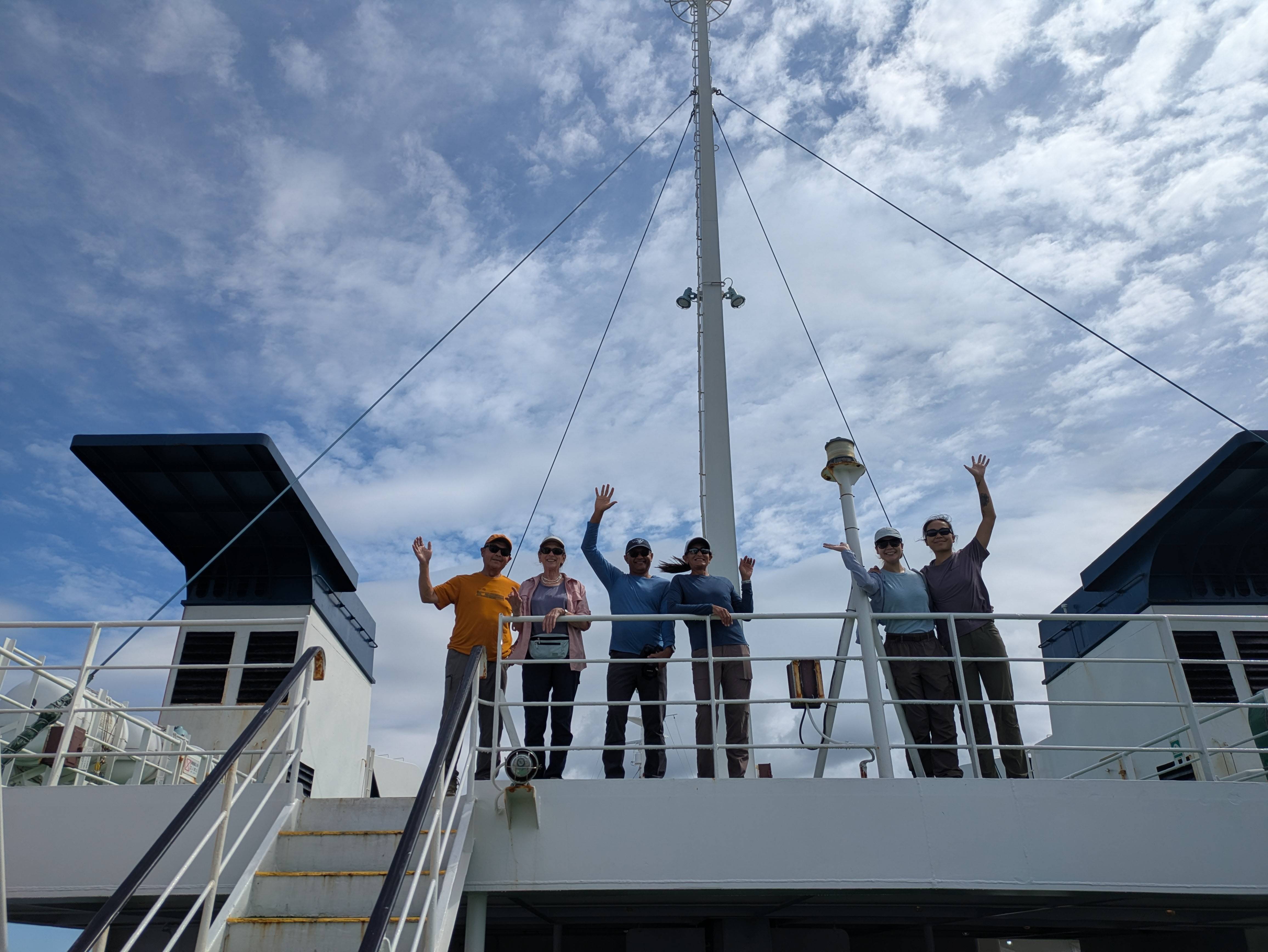 A group stands alongside the railing of a ferry, waving to the camera. The ferry is the Heartland Ferry, which carries guests between Wakkanai and Rebun Island in Hokkaido.