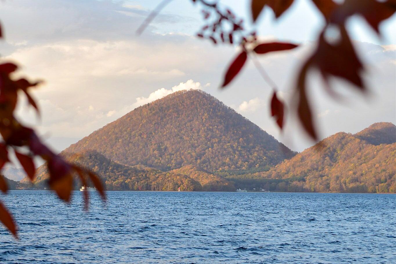 A view of Nakajima Island in Lake Toya in autumn, framed by autumn leaves.
