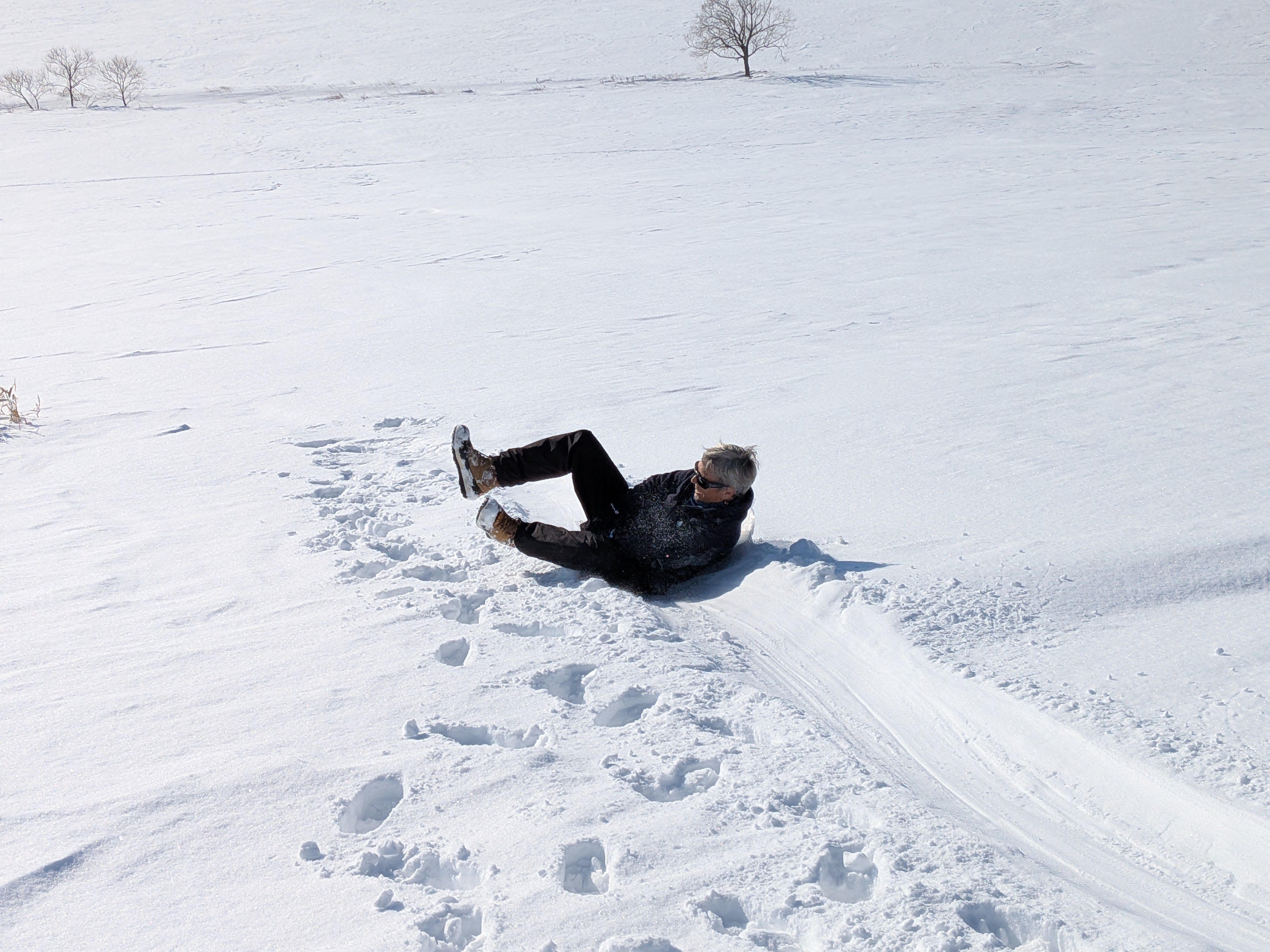 A woman sleds downhill on a snowy hill, using a small hip sled (the user sits on the sled and holds on to a handle between their legs). It looks like she is having a lot of fun.