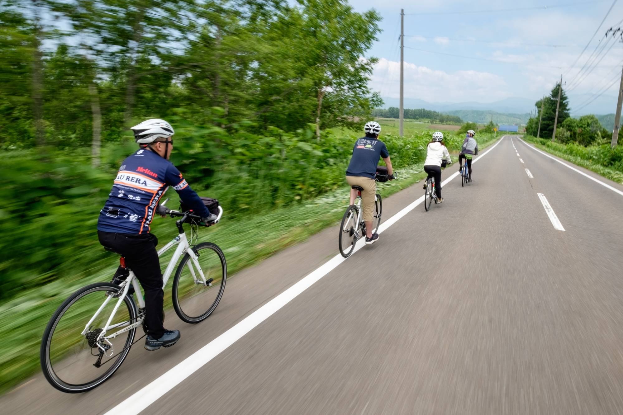 A guided cycling tour rides along a rural road surrounded by greenery.