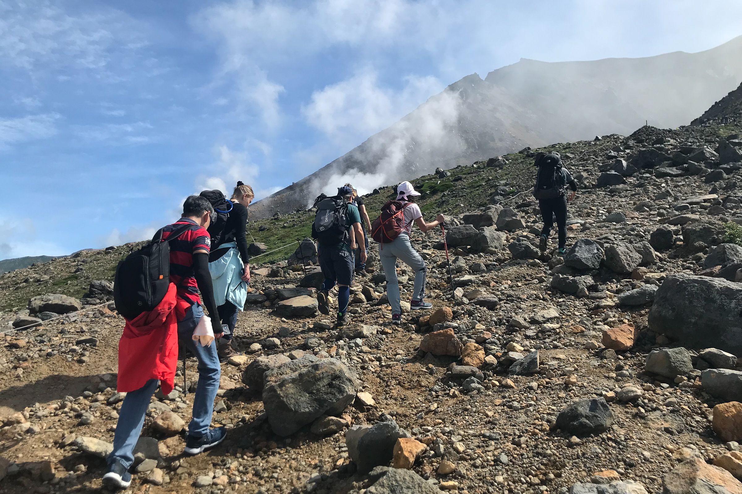 A group of hikers ascend a rocky mountain slope on a sunny day.