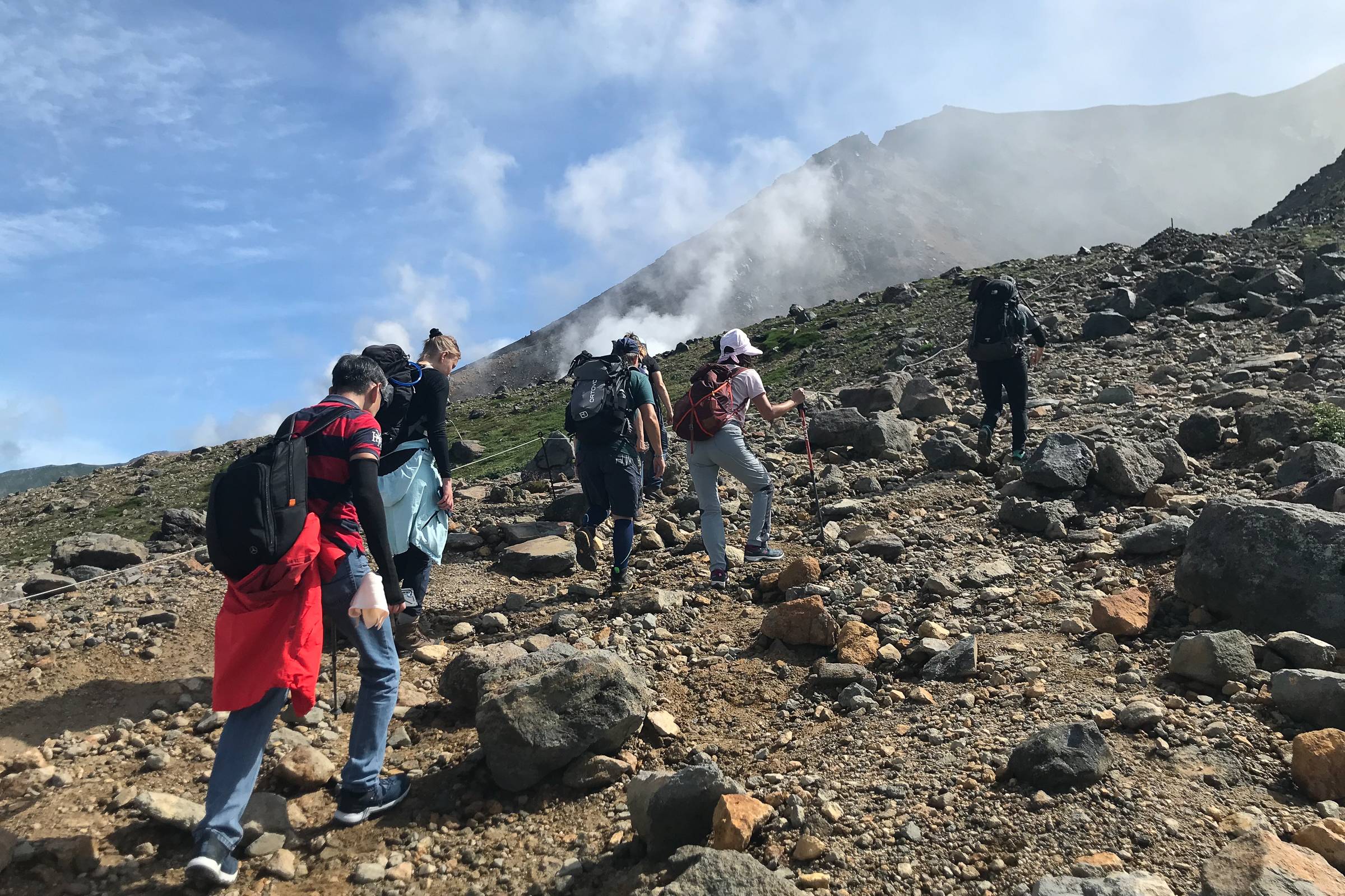 A group of hikers ascend a rocky mountain slope on a sunny day.