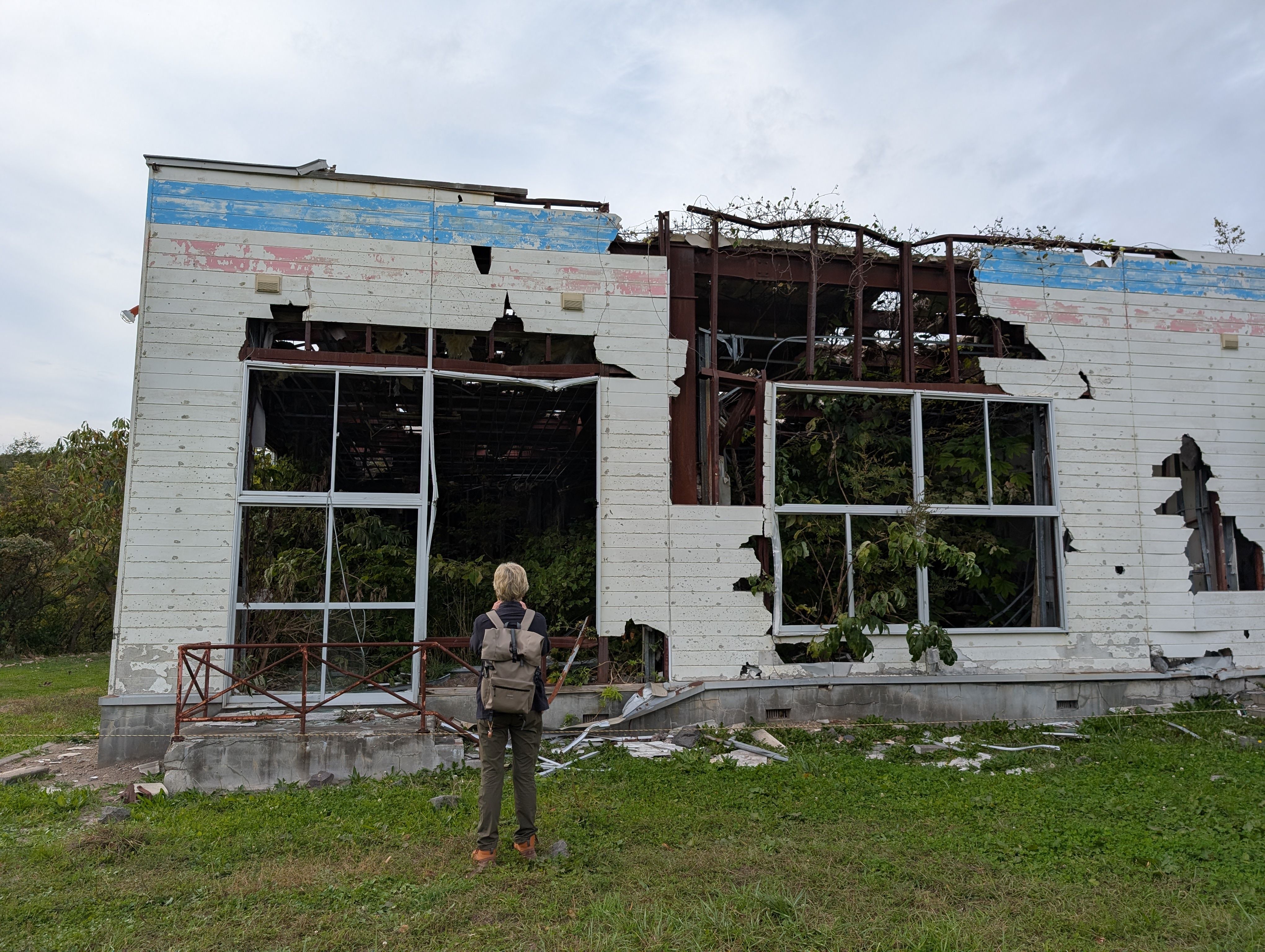 A woman stands outside the ruins of a kindergarten destroyed by a volcanic explosion in 2000. The walls are pockmarked by damage and vegetation is growing inside.