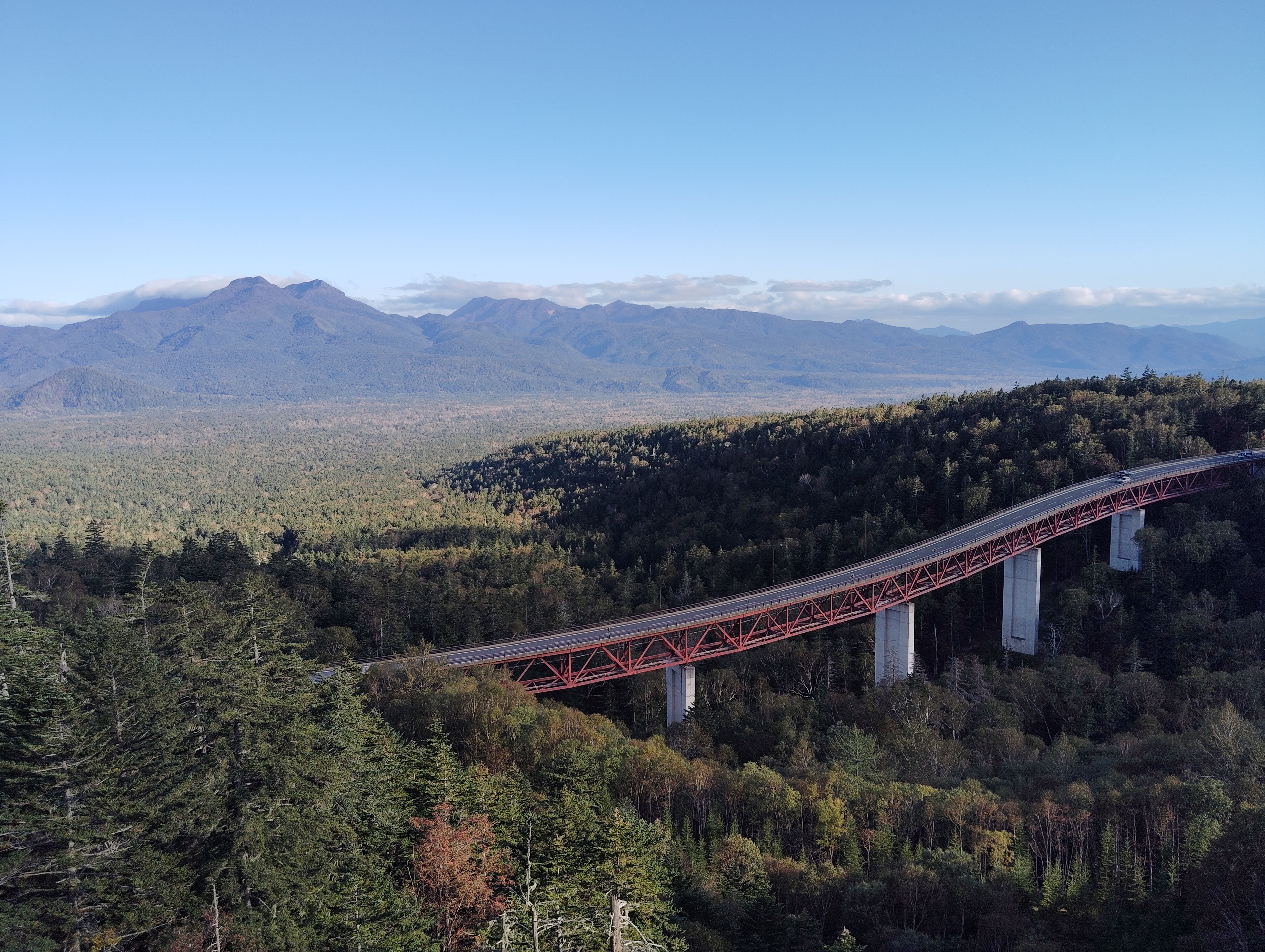 A view of a road spanning Mikuni Pass in Hokkaido. It is a beautiful day and the bridge spans a valley far below. It's a beautiful sunny day and mountains are visible on the horizon.