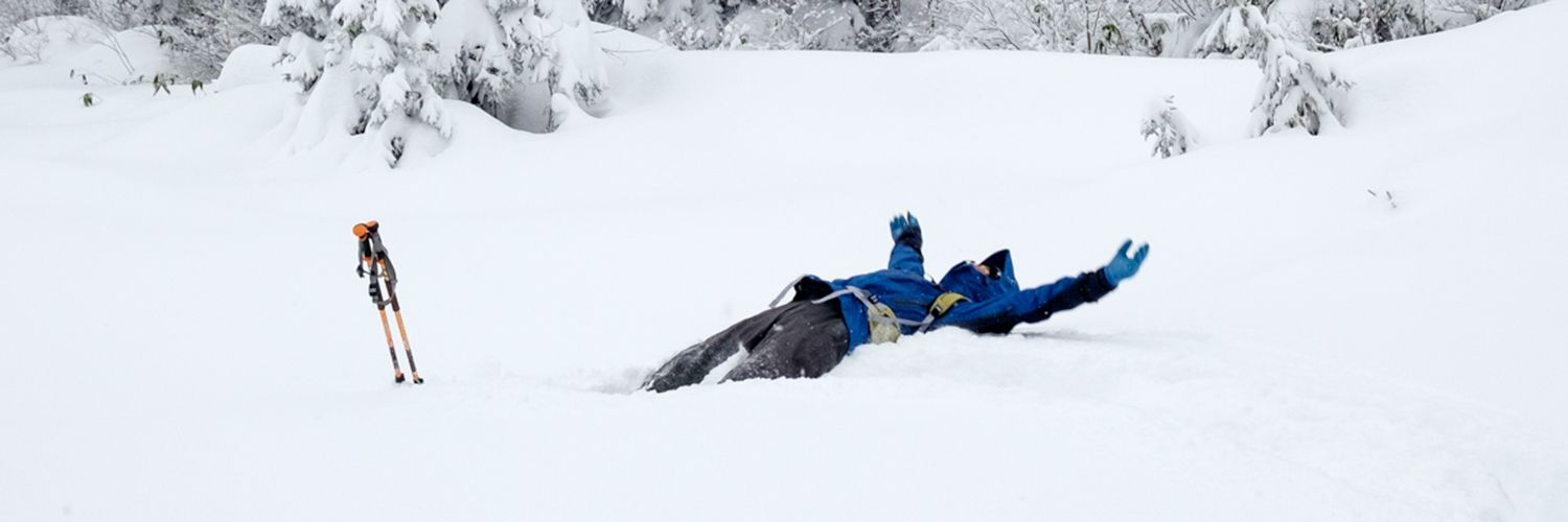 A snowshoer falls backwards into the snow. The photo captures the split second before they disappear into the snow.